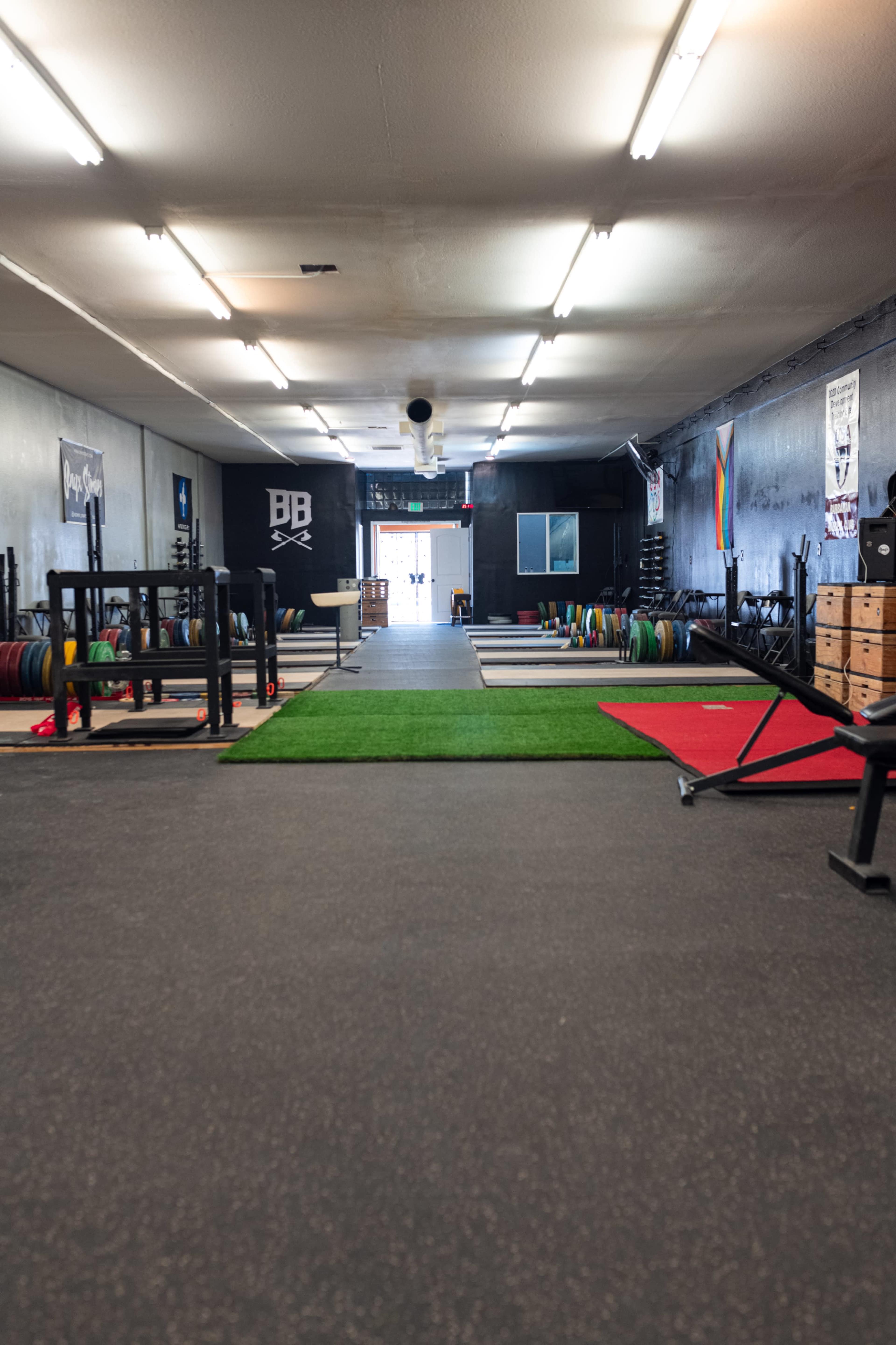 An empty gym space with various lifting equipment and colorful weight plates arranged on the floor.