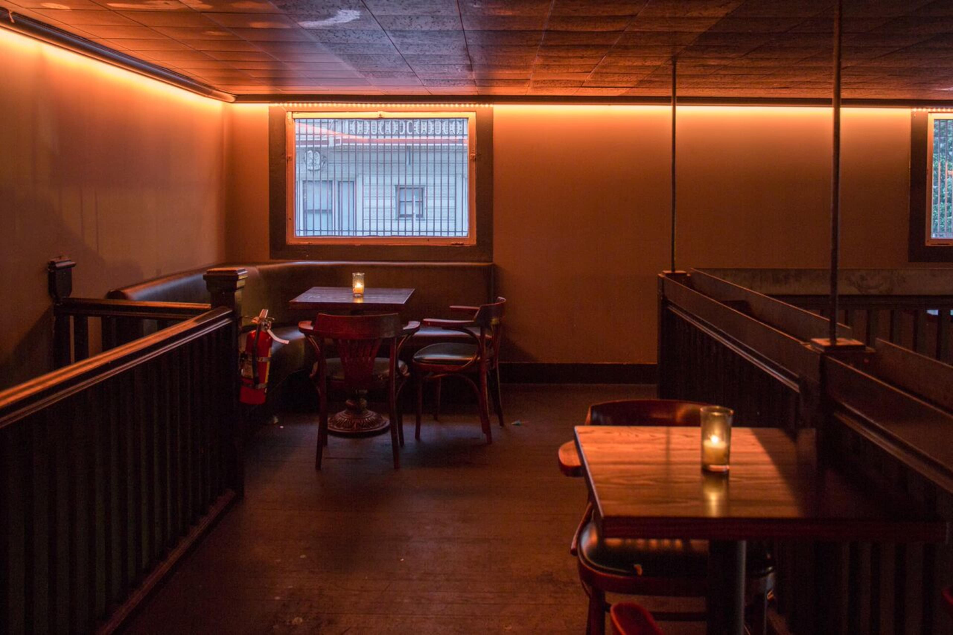 A dimly lit interior of a bar with wooden tables and chairs near a window.