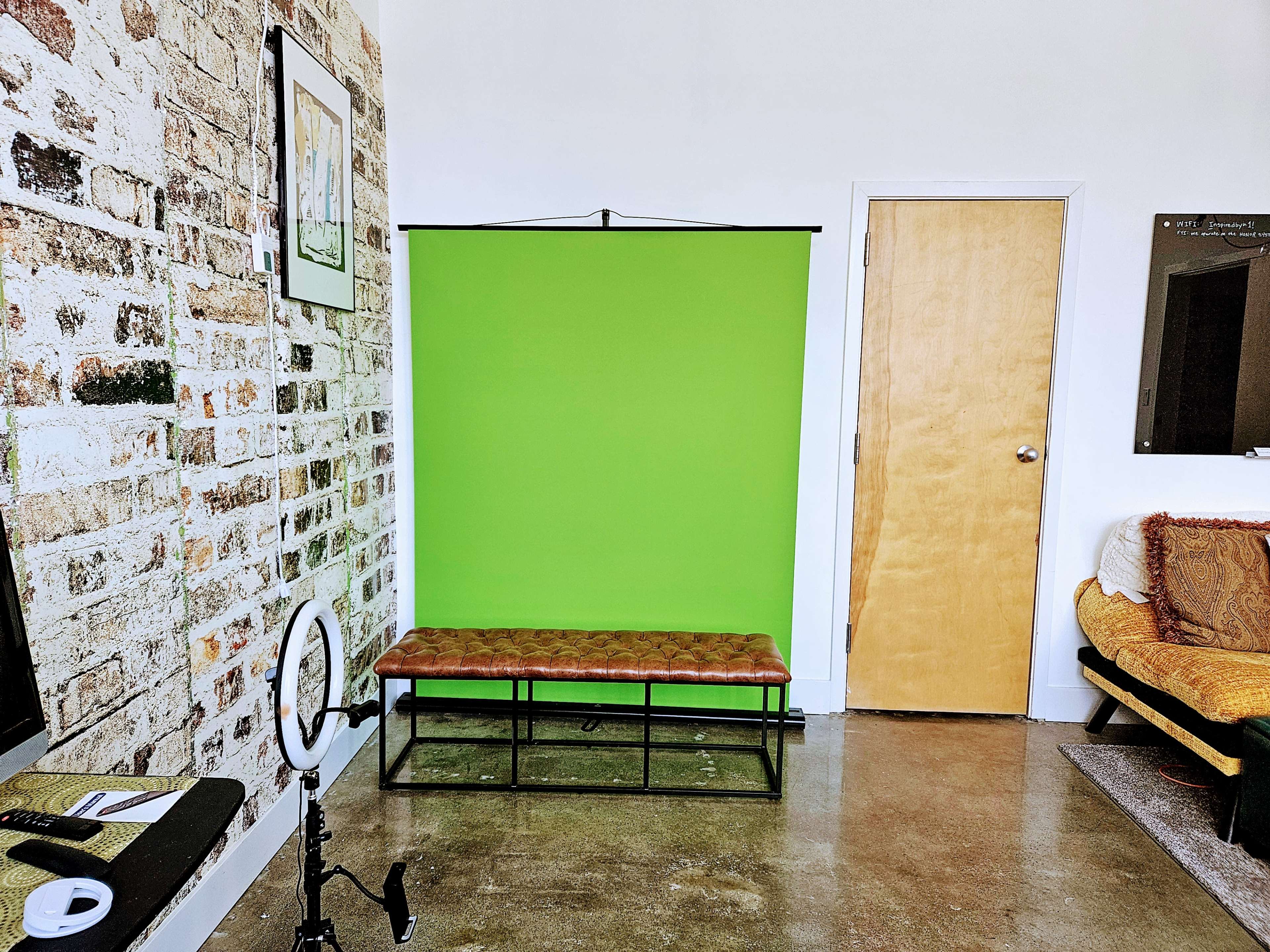 A room with a green backdrop on a stand, a brown bench against the wall, and a door leading to another area.