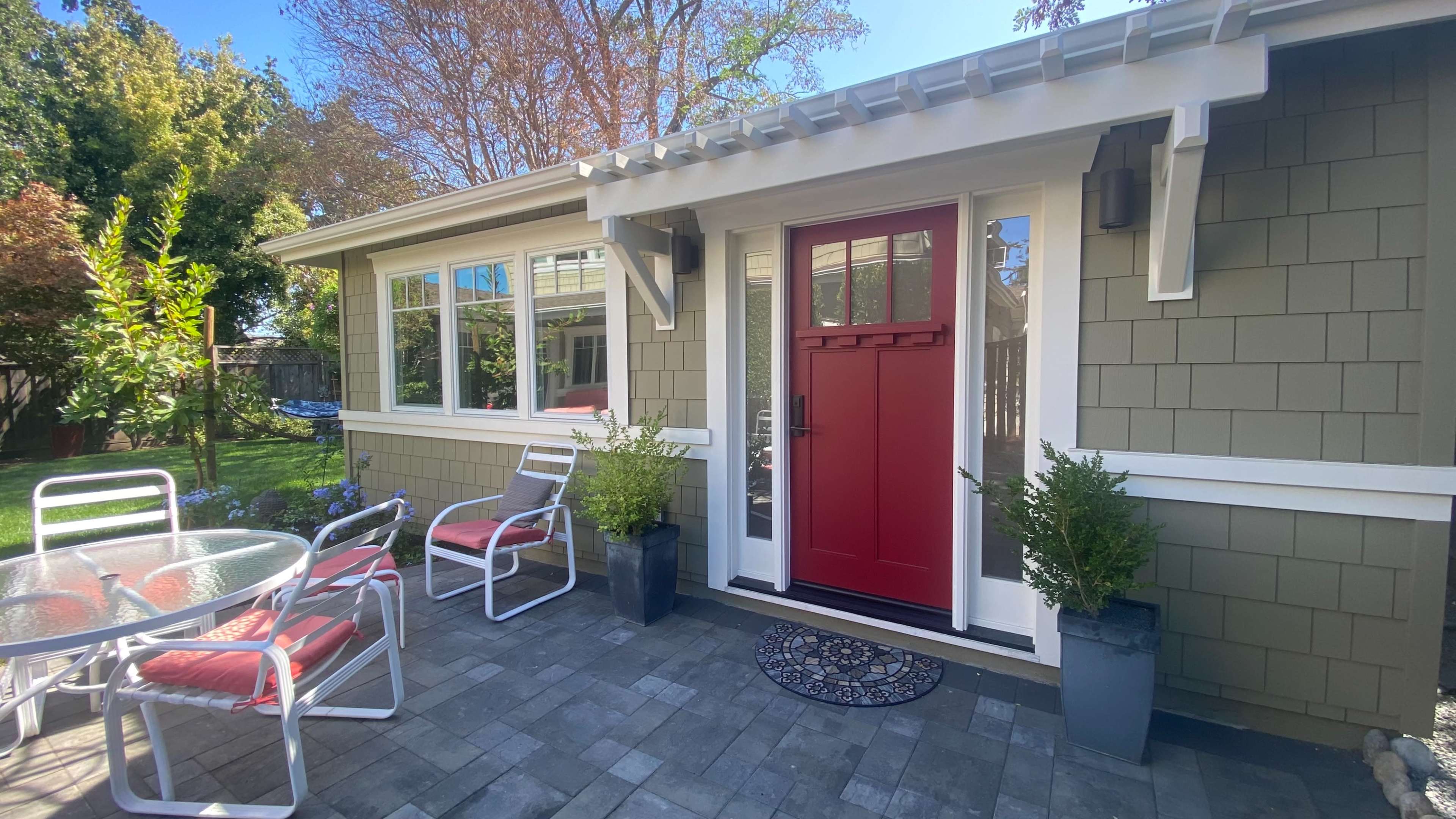 A charming outdoor patio area featuring a red front door, a round table with four chairs, and potted plants beside the entrance of a house.