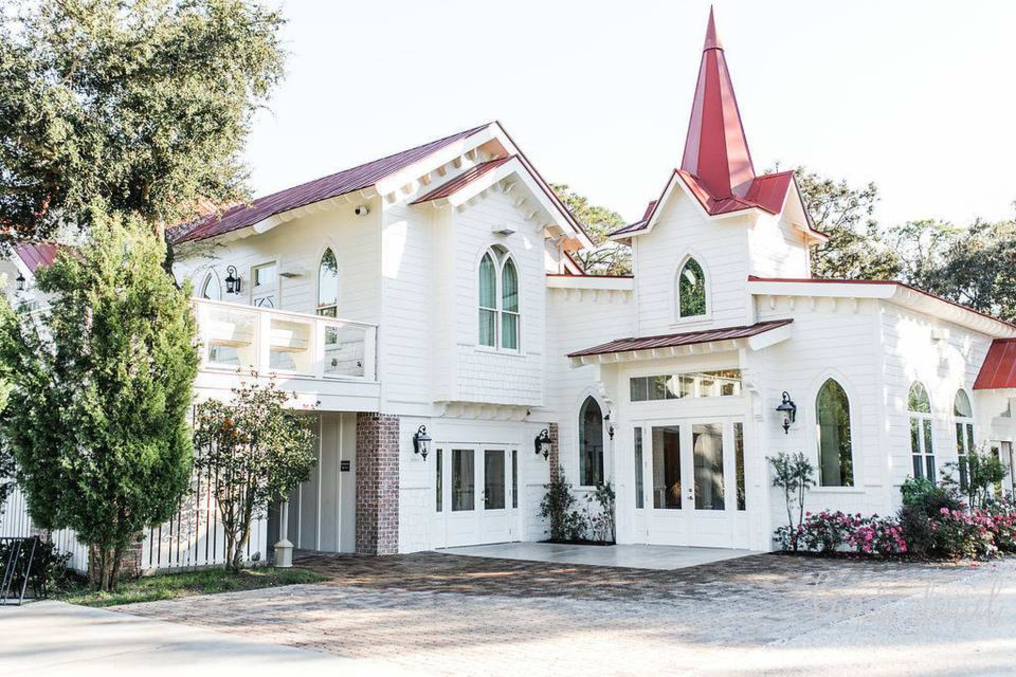 The image shows a two-story white house with a red roof and a tall spire, featuring large windows and a landscaped front yard.