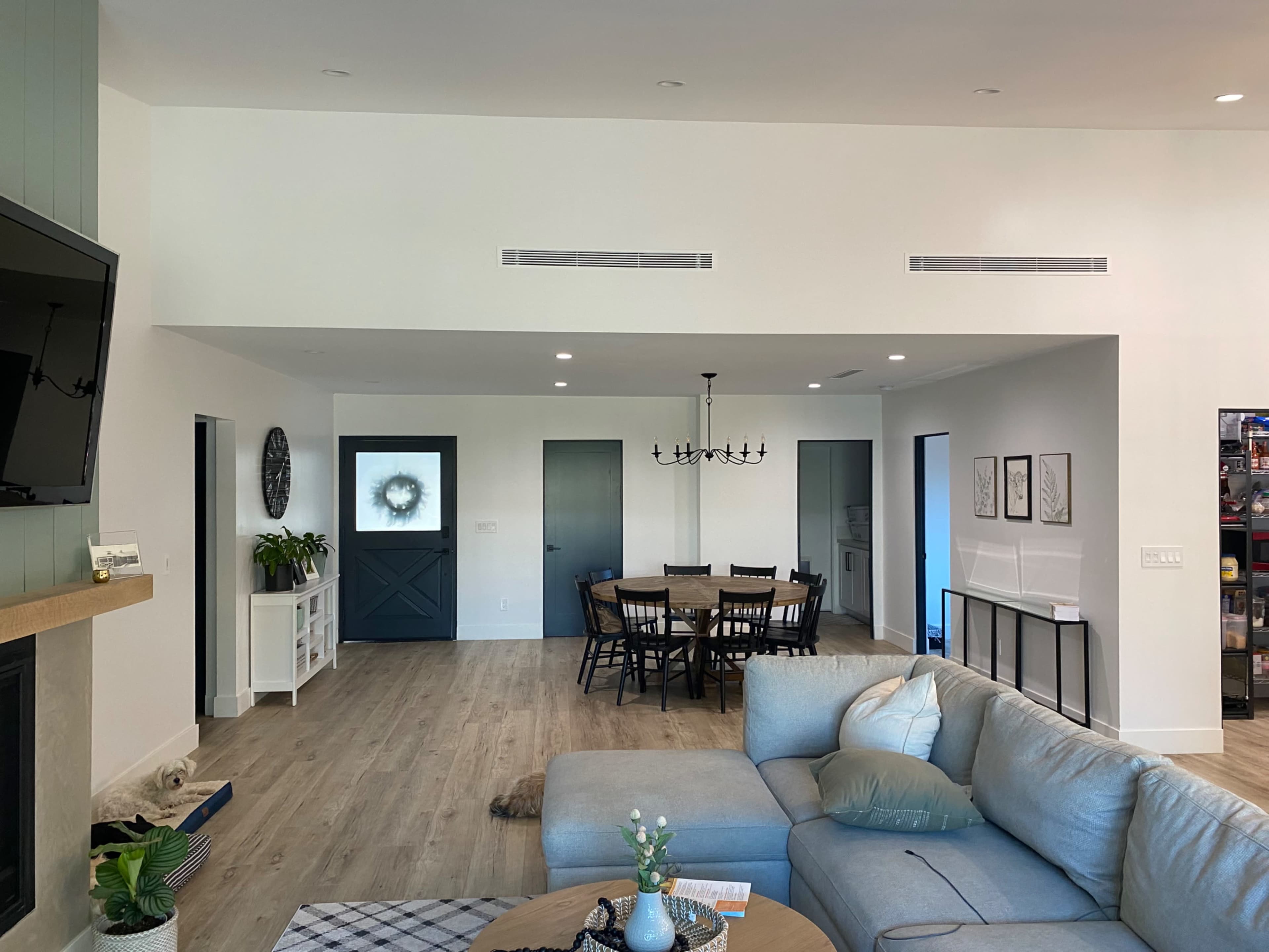 A modern open-concept living area featuring a sectional sofa, a dining table with chairs, and a doorway leading to a kitchen space.