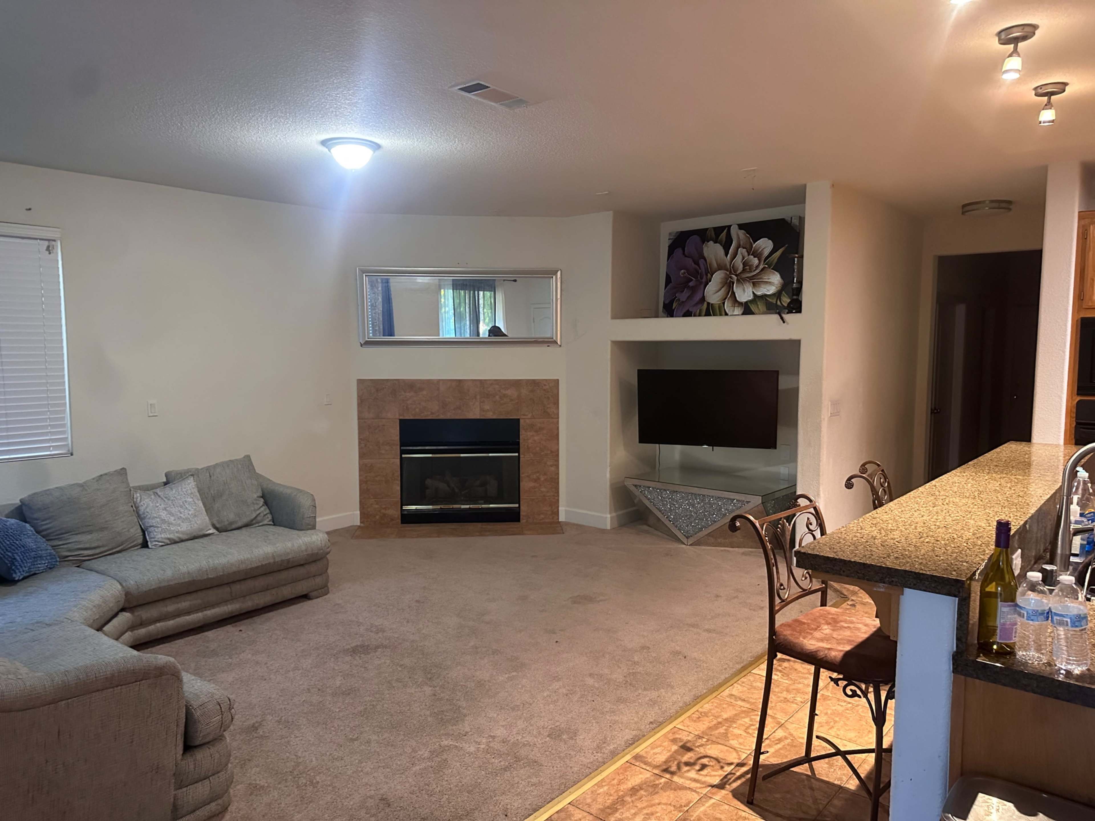 A living room with a sectional sofa, a fireplace, a mounted television, and a kitchen counter with bar stools.