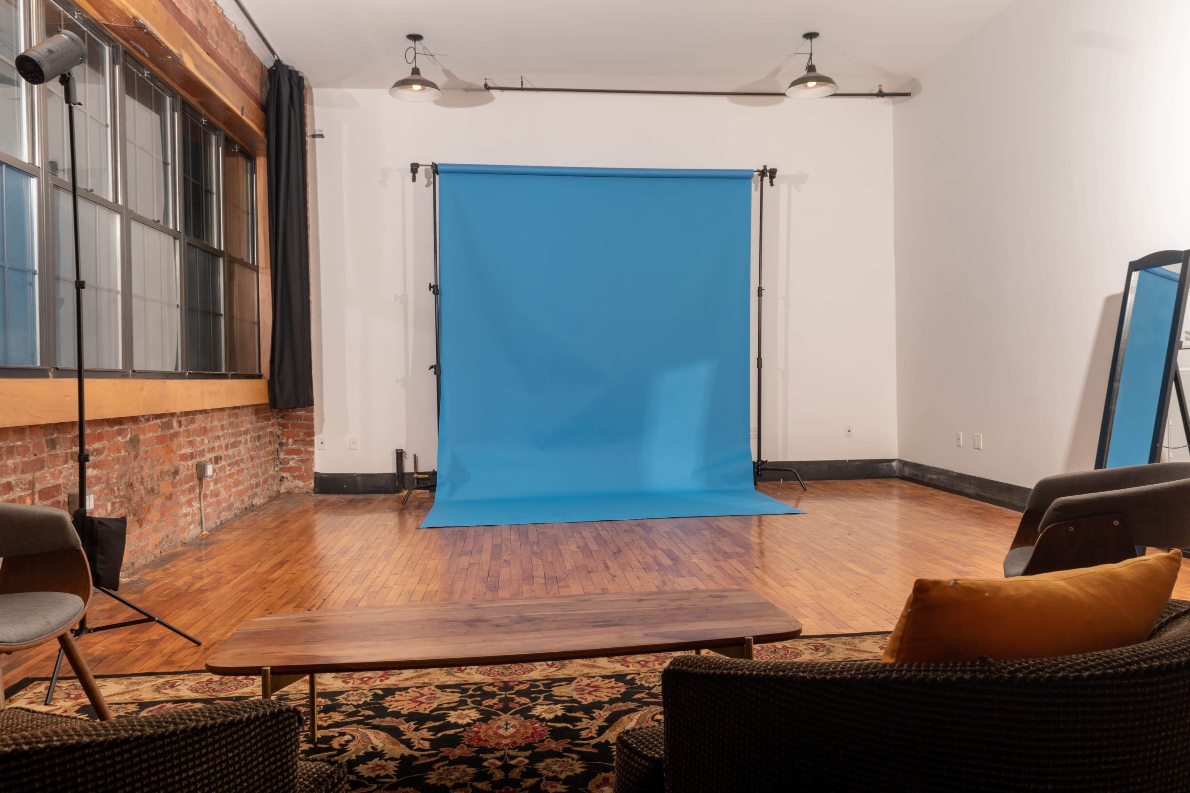 A photography studio with a blue backdrop, wooden flooring, and seating arranged in front of the backdrop.