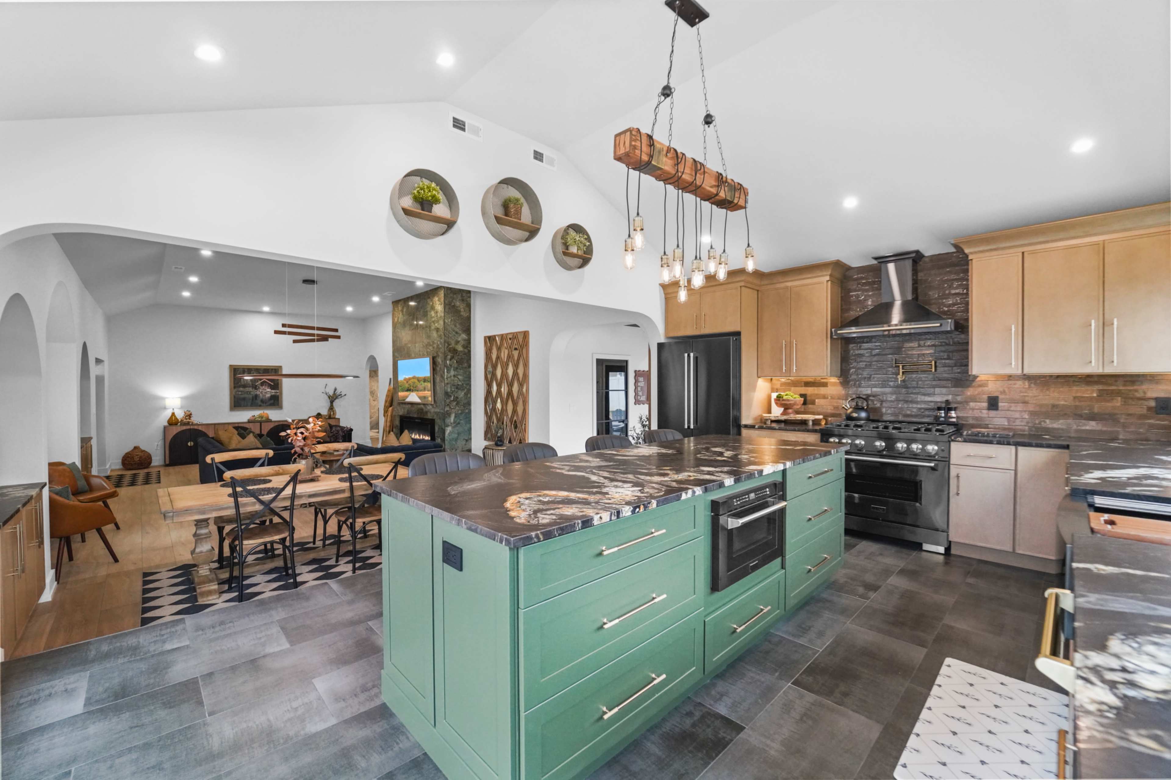 The image shows a modern kitchen with a large green island, stainless steel appliances, and an open layout leading to a dining area in the background.