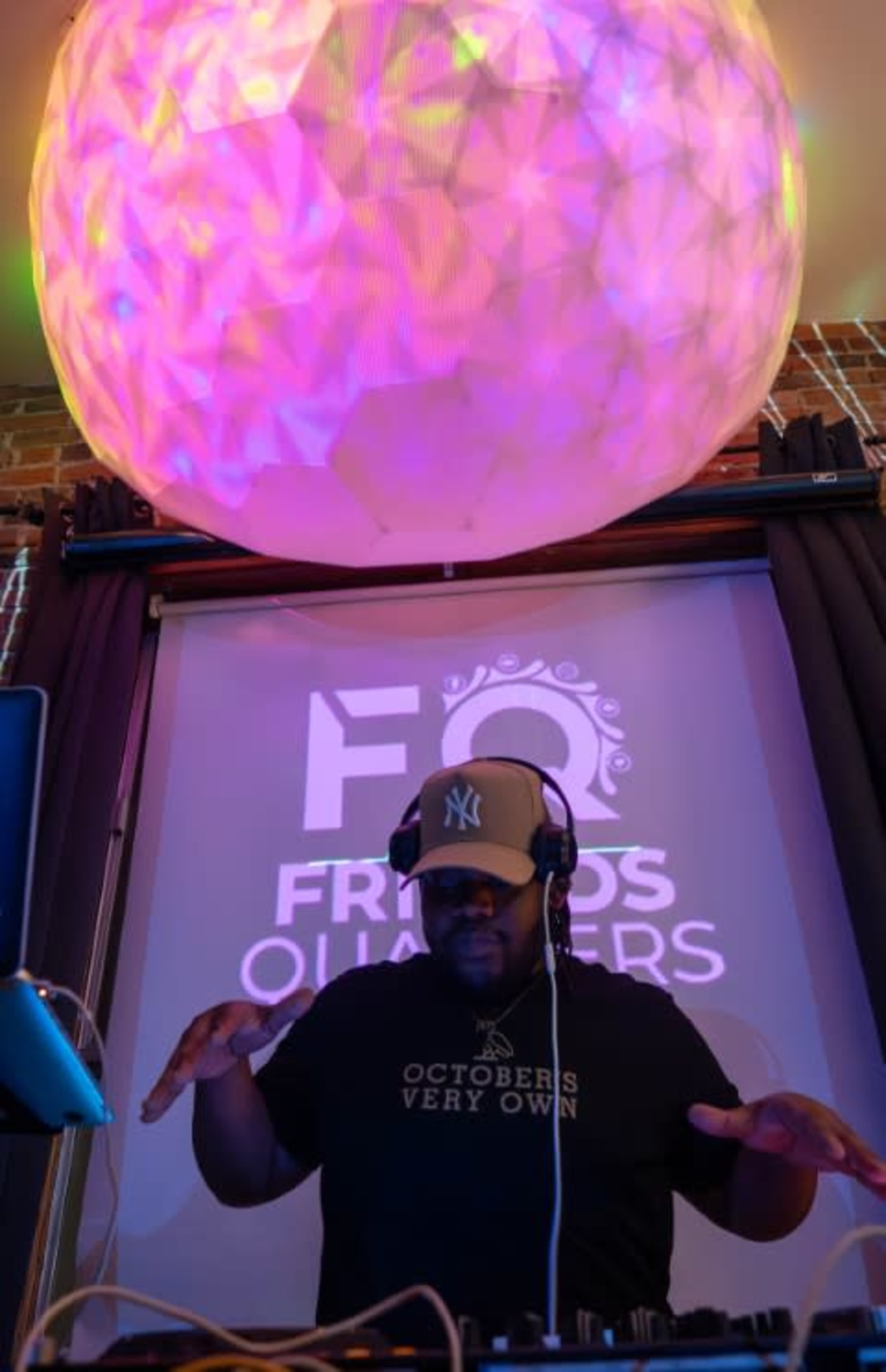 A DJ with headphones is performing at a venue, focused on mixing music while colorful lighting illuminates the space above him.