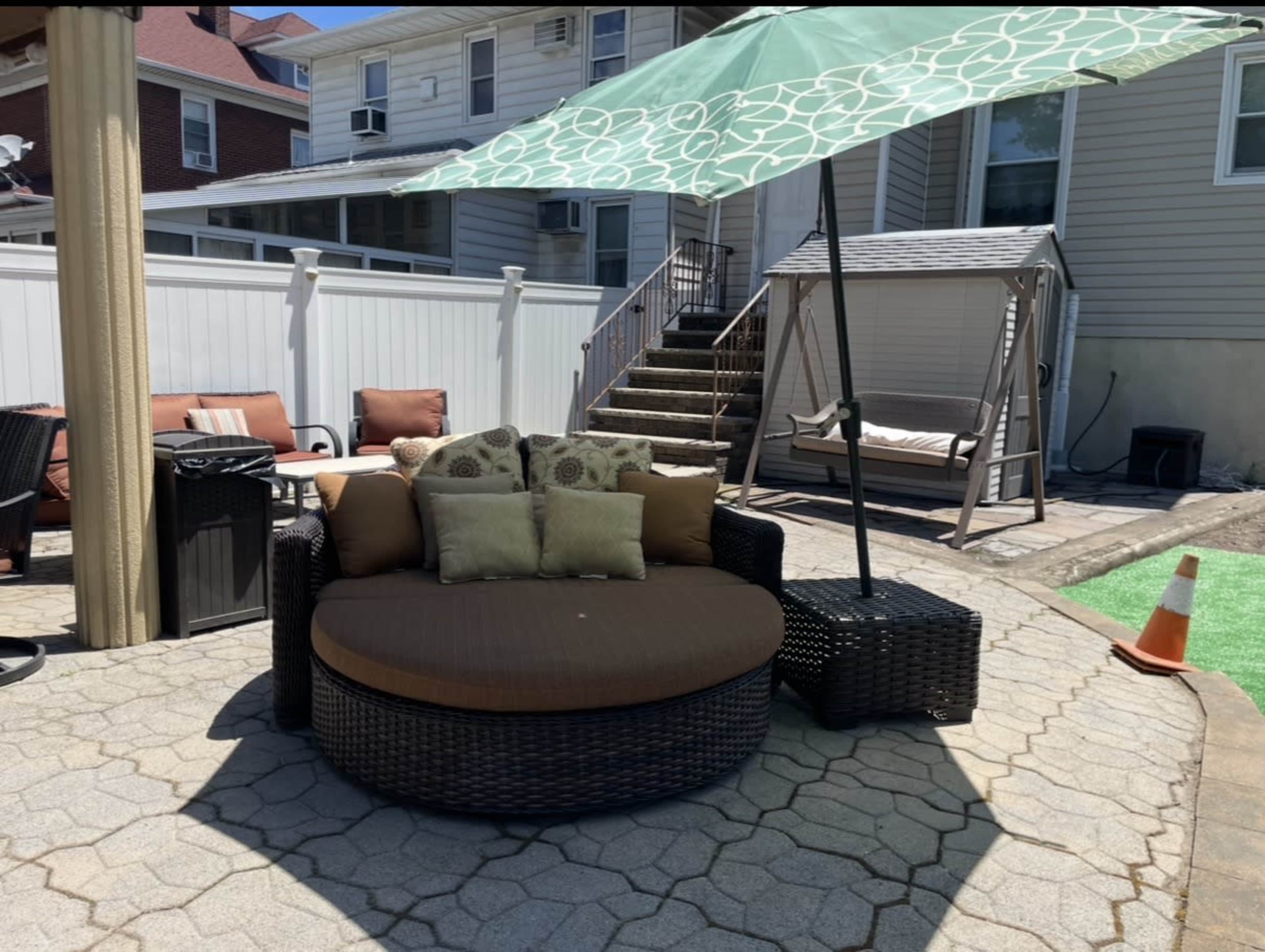 The image shows a circular outdoor seating area with a large umbrella, surrounded by a paved patio and a few chairs in the background.