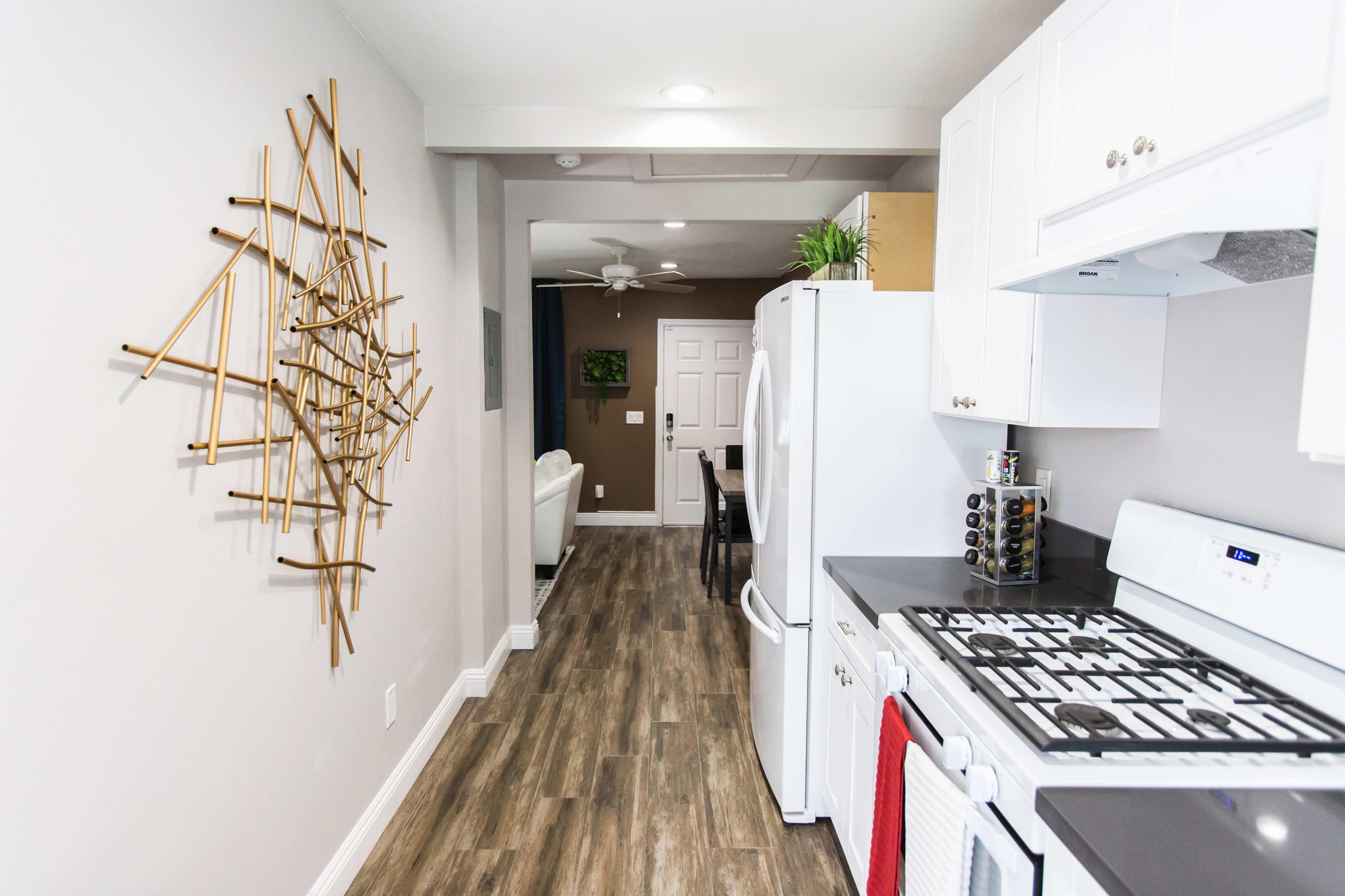 A modern kitchen with a white refrigerator and stove, complemented by a decorative wall piece and a view into a dining area with light-colored furniture.