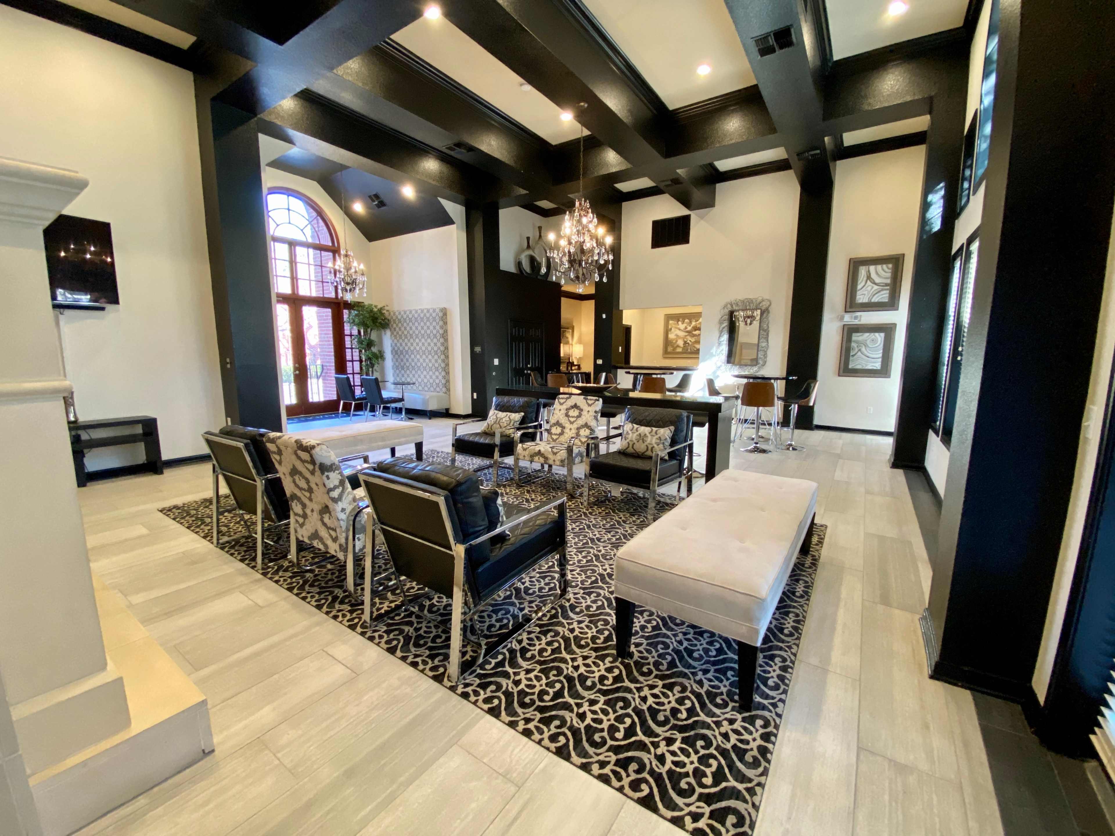 A spacious lounge area with black wooden beams, modern seating arrangements, and a large area rug featuring an intricate pattern.