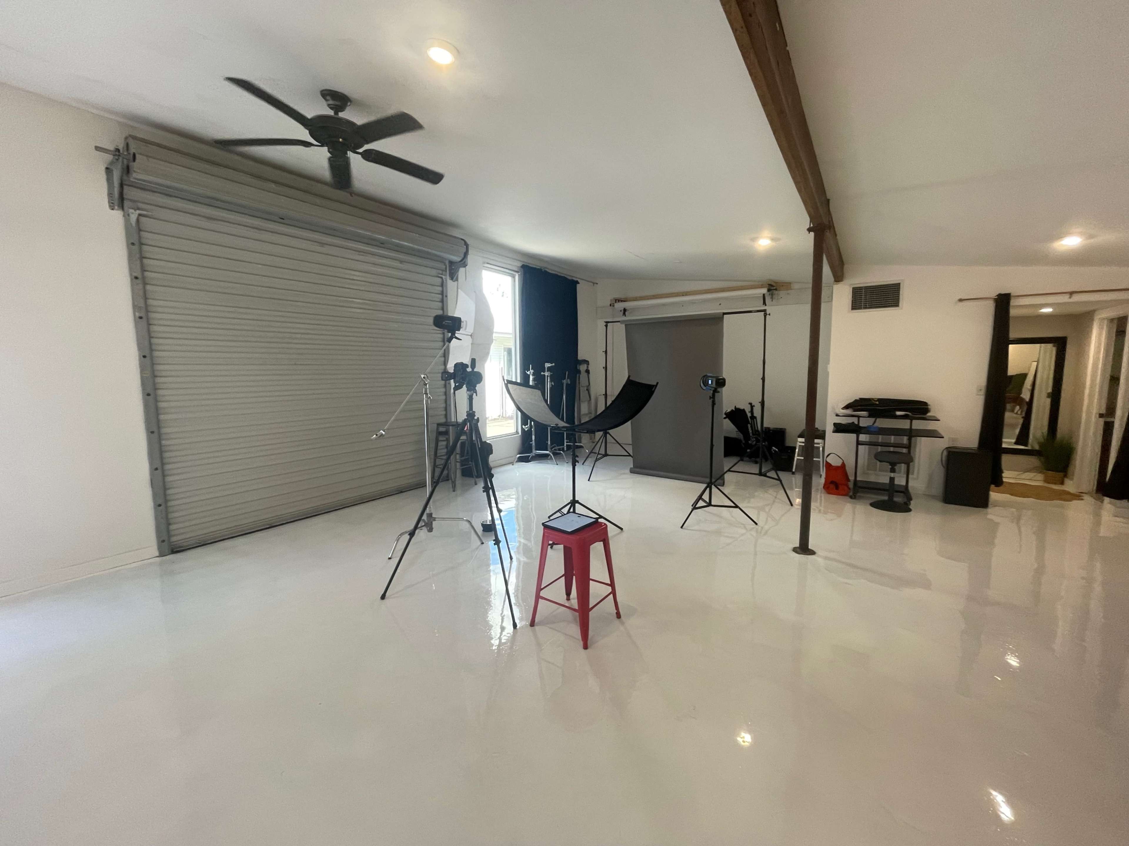 A well-lit studio space with photography equipment, including tripods, softboxes, and a backdrop setup, along with a pink stool in the center.