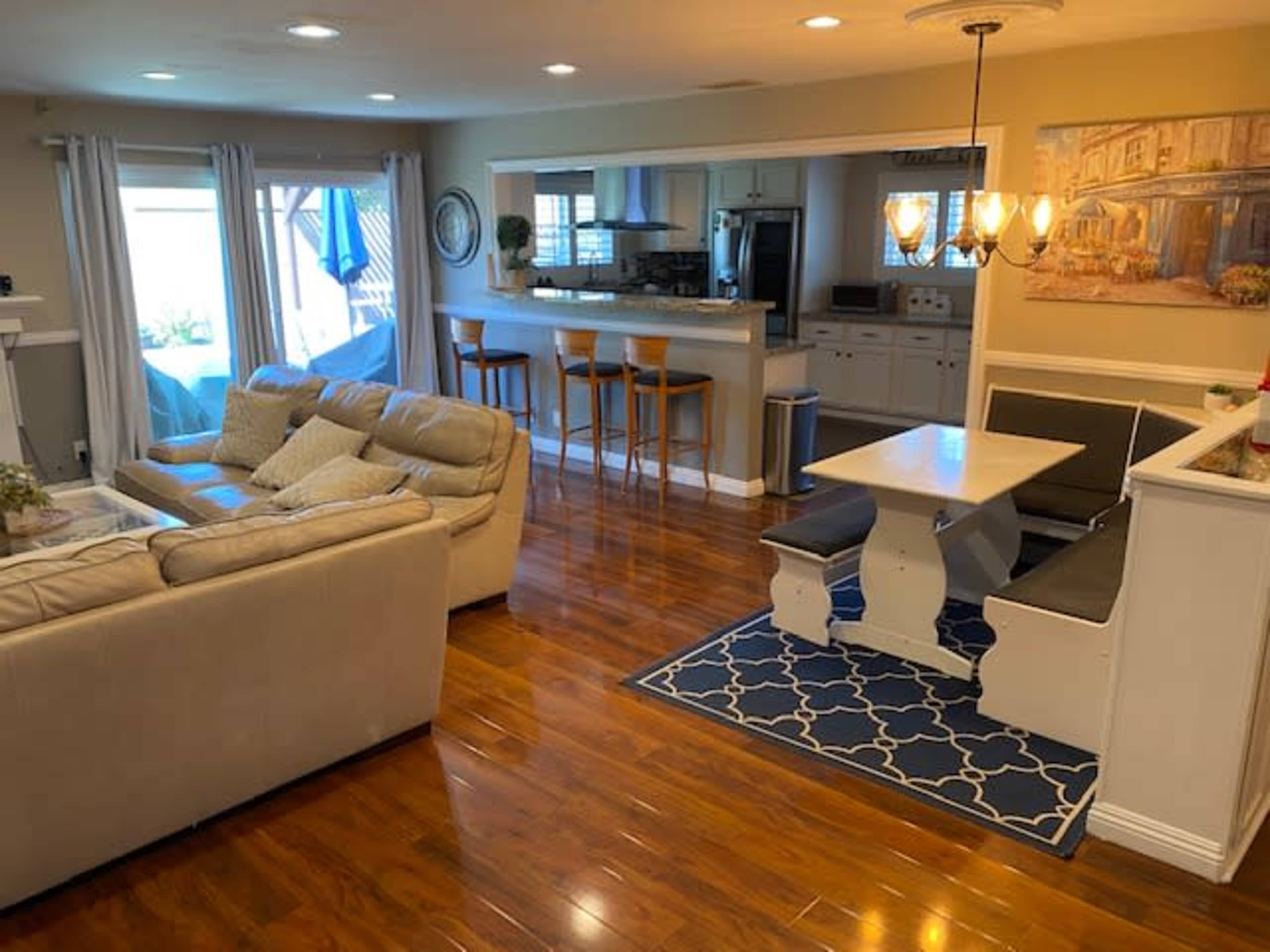 A spacious living area with a beige couch, a dining nook with a built-in bench, hardwood floors, and a kitchen area in the background.