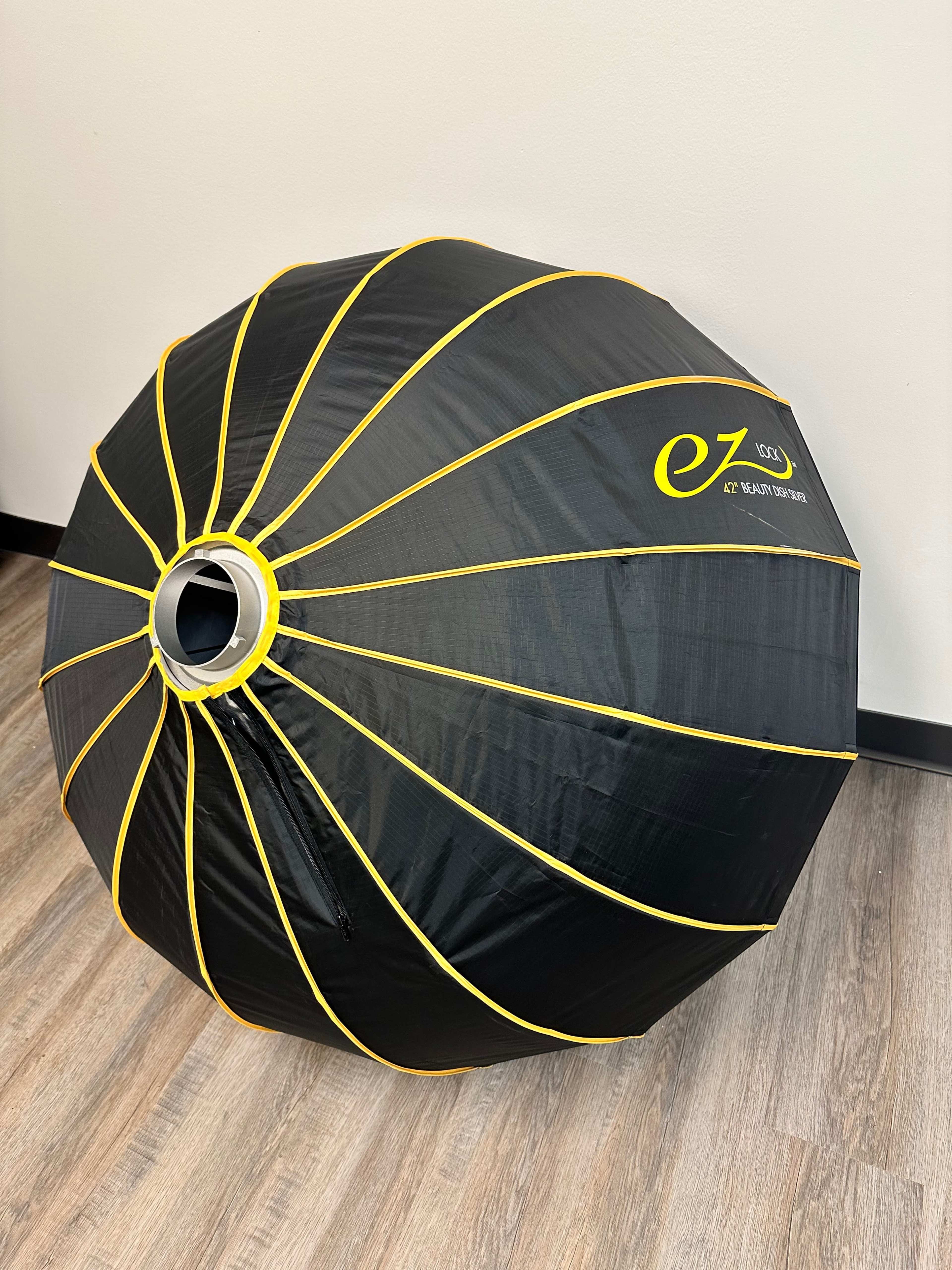 A large black and yellow collapsible fabric light modifier sits on a wooden floor against a plain wall.