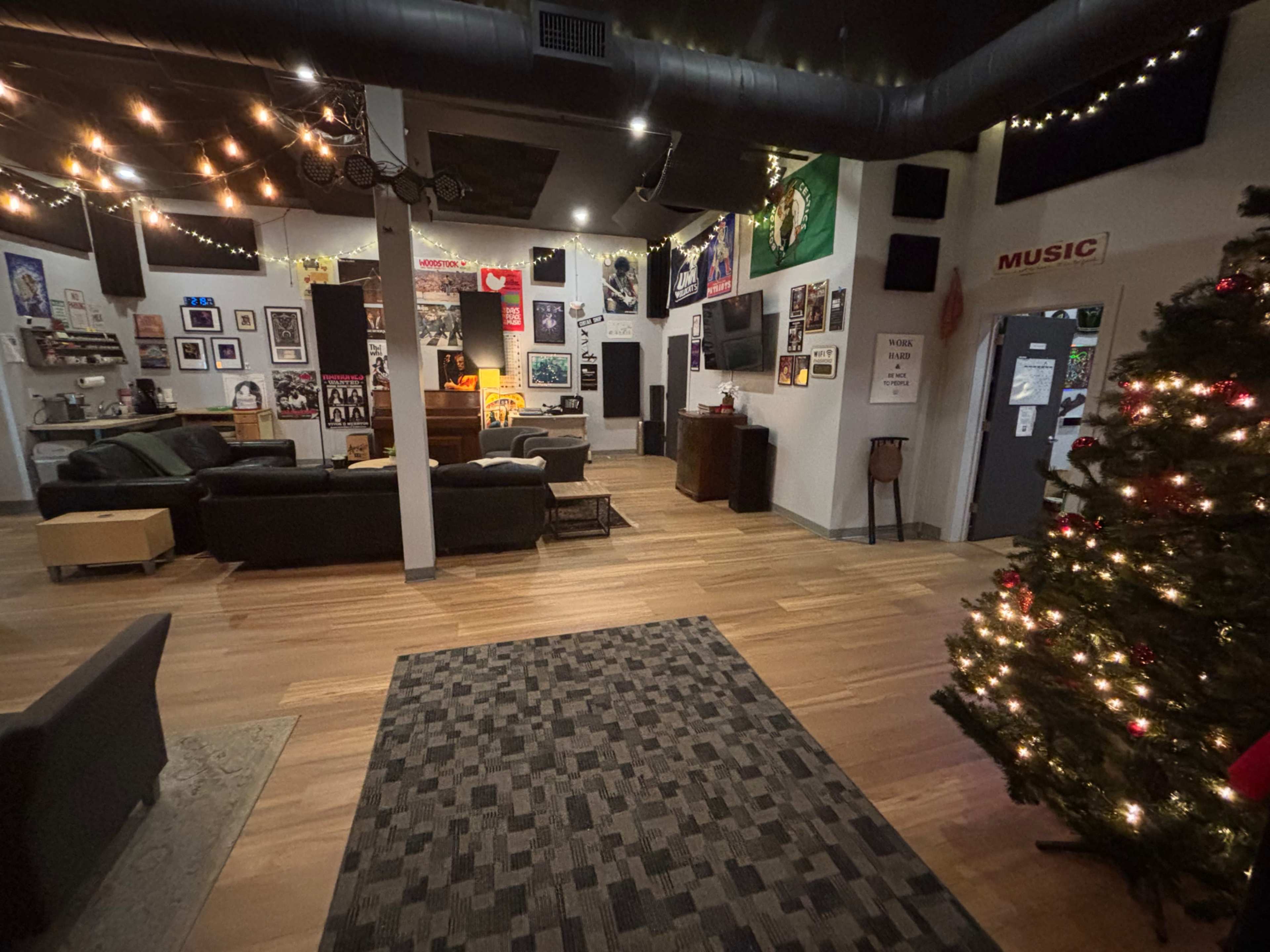 The image shows a spacious lounge area with hardwood flooring, decorated with music-themed wall art, a large sofa, and a Christmas tree in the corner.