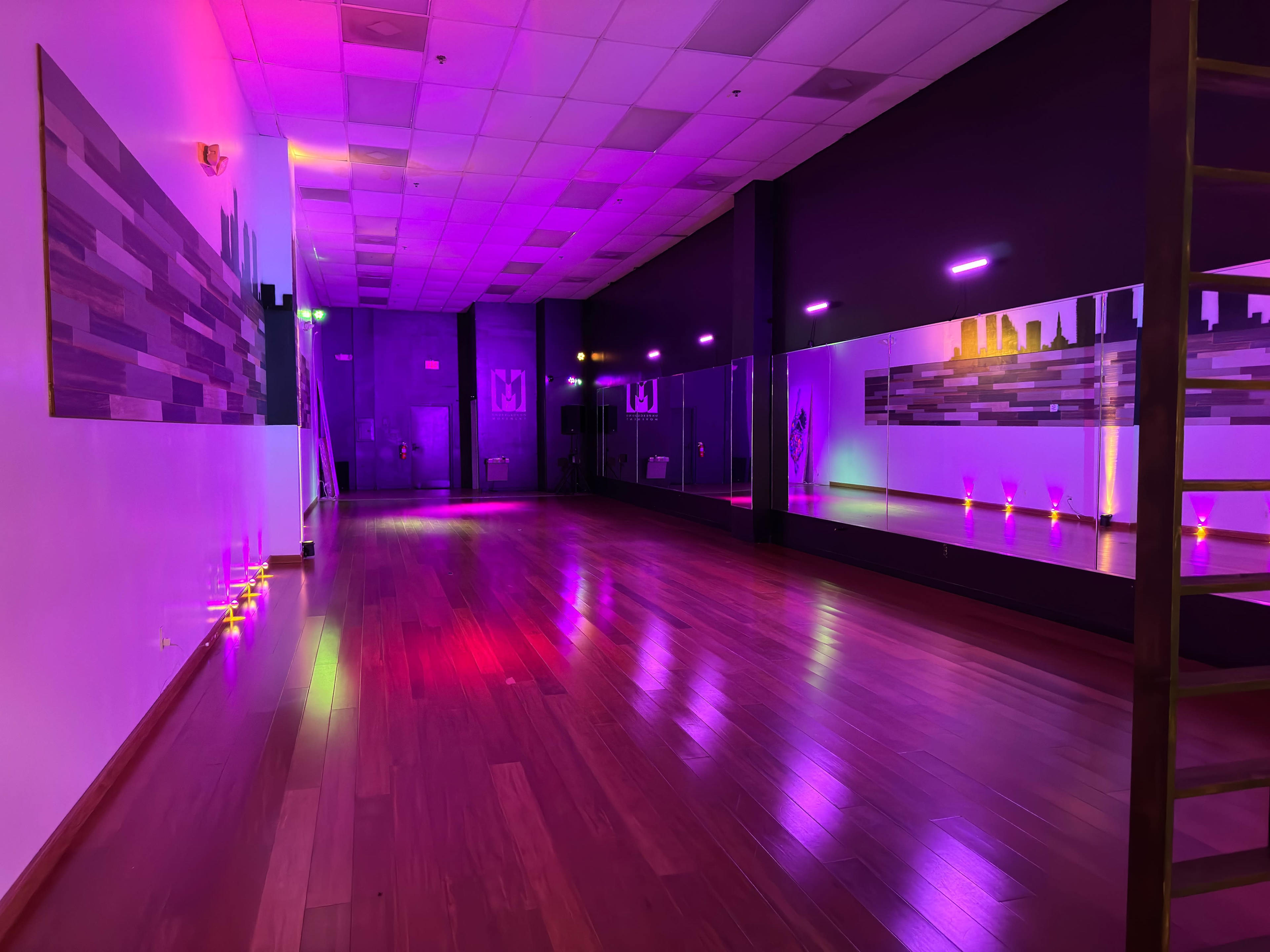 An empty dance studio with wooden floors, mirrored walls, and colorful lighting.
