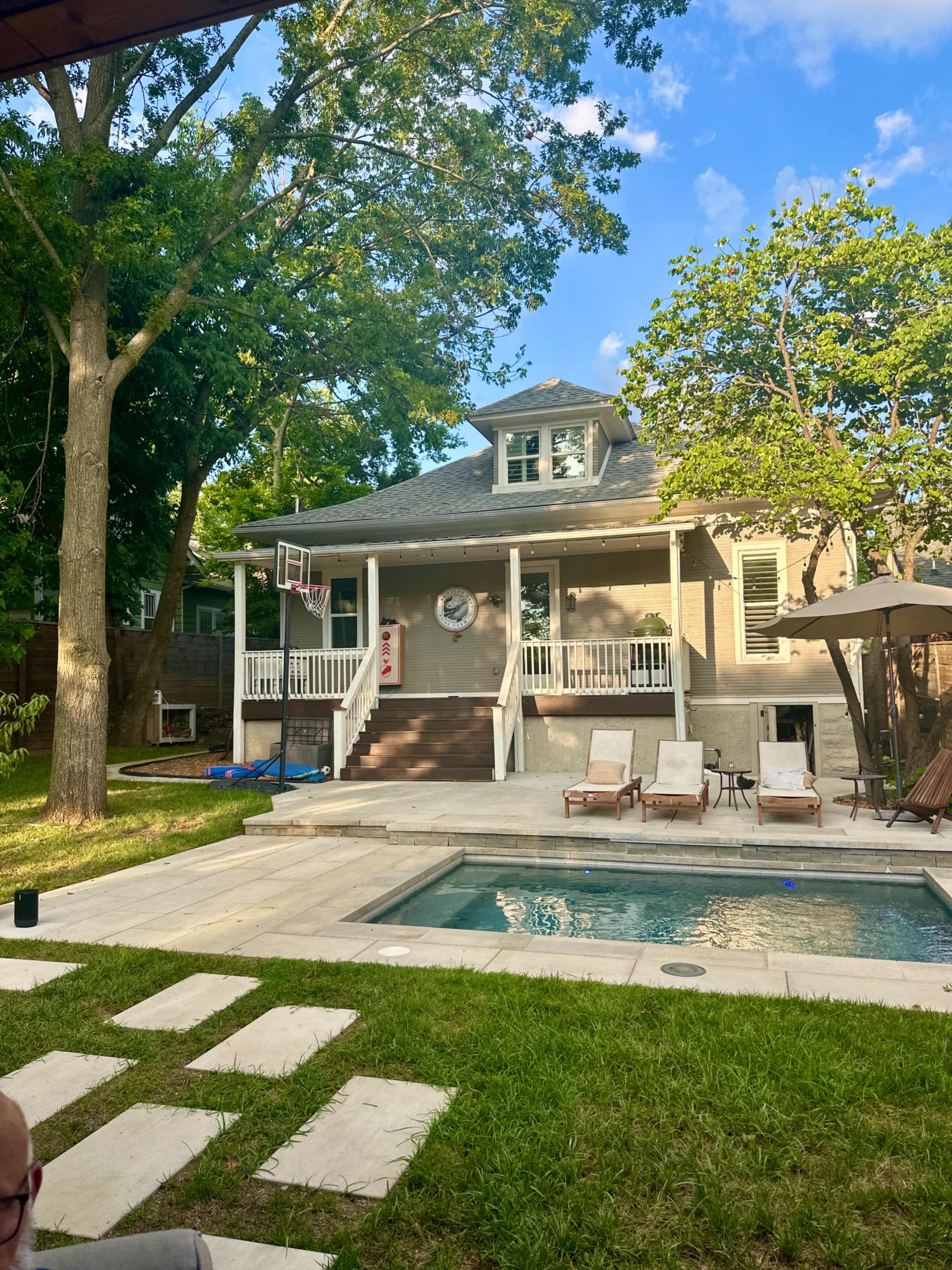 The image shows a residential backyard with a swimming pool, lounge chairs, and a two-story house surrounded by trees.