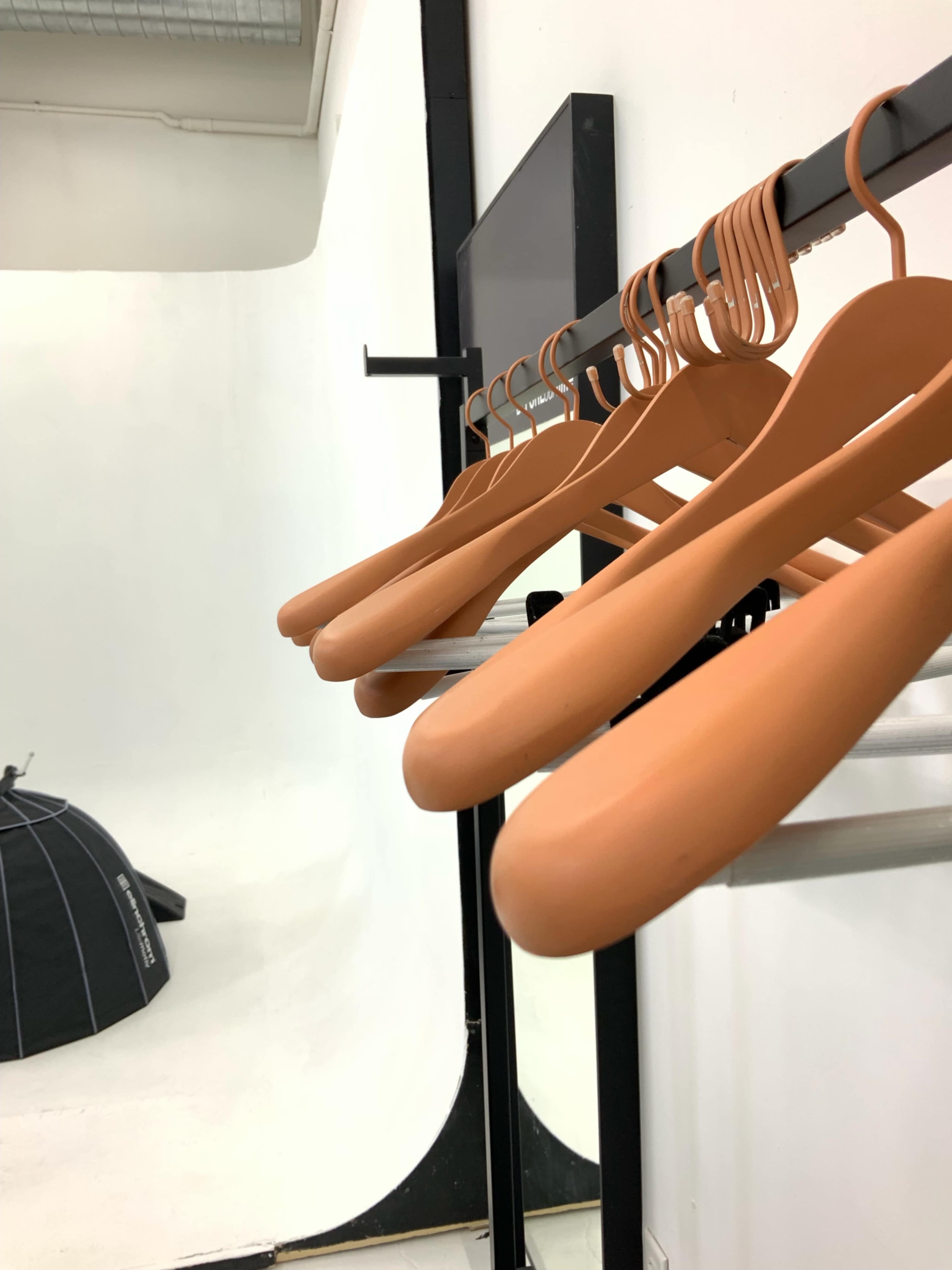 The image shows a row of brown hangers hanging on a rack in a studio setting with a blank white background.