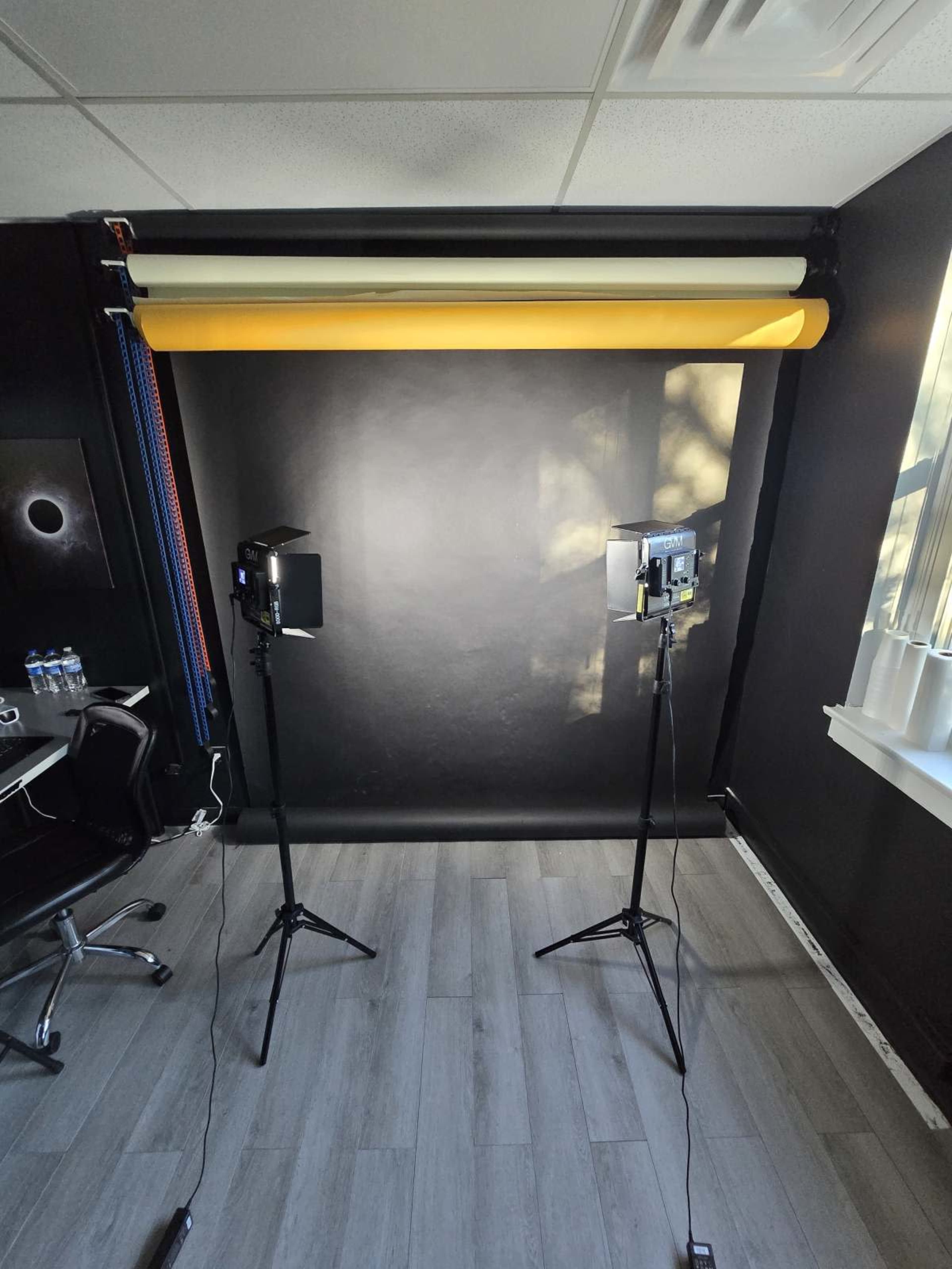 A photography studio setup with two lights on stands facing a black backdrop and a roll of yellow paper.