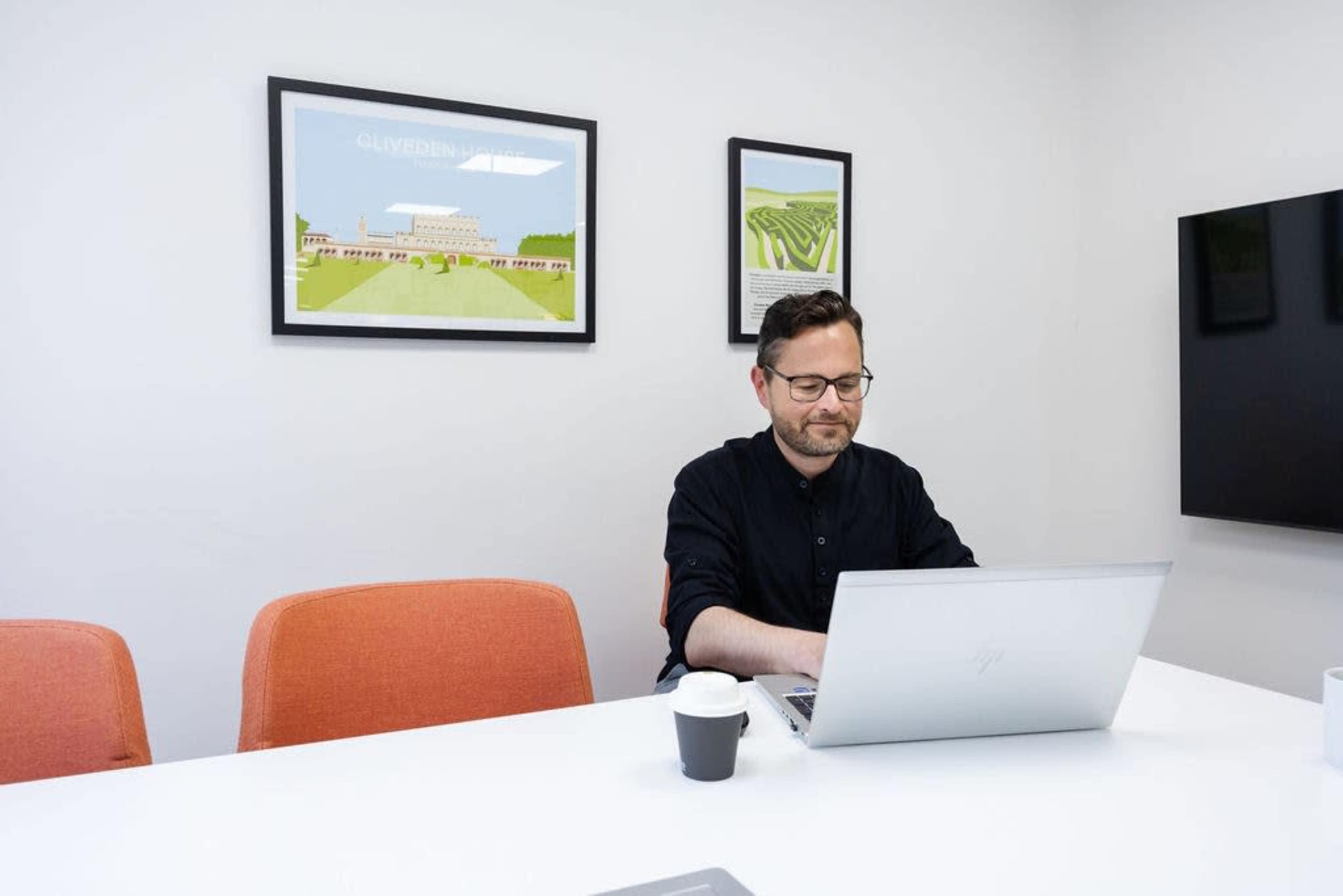 A man works on a laptop at a white table in a conference room with artwork on the walls.