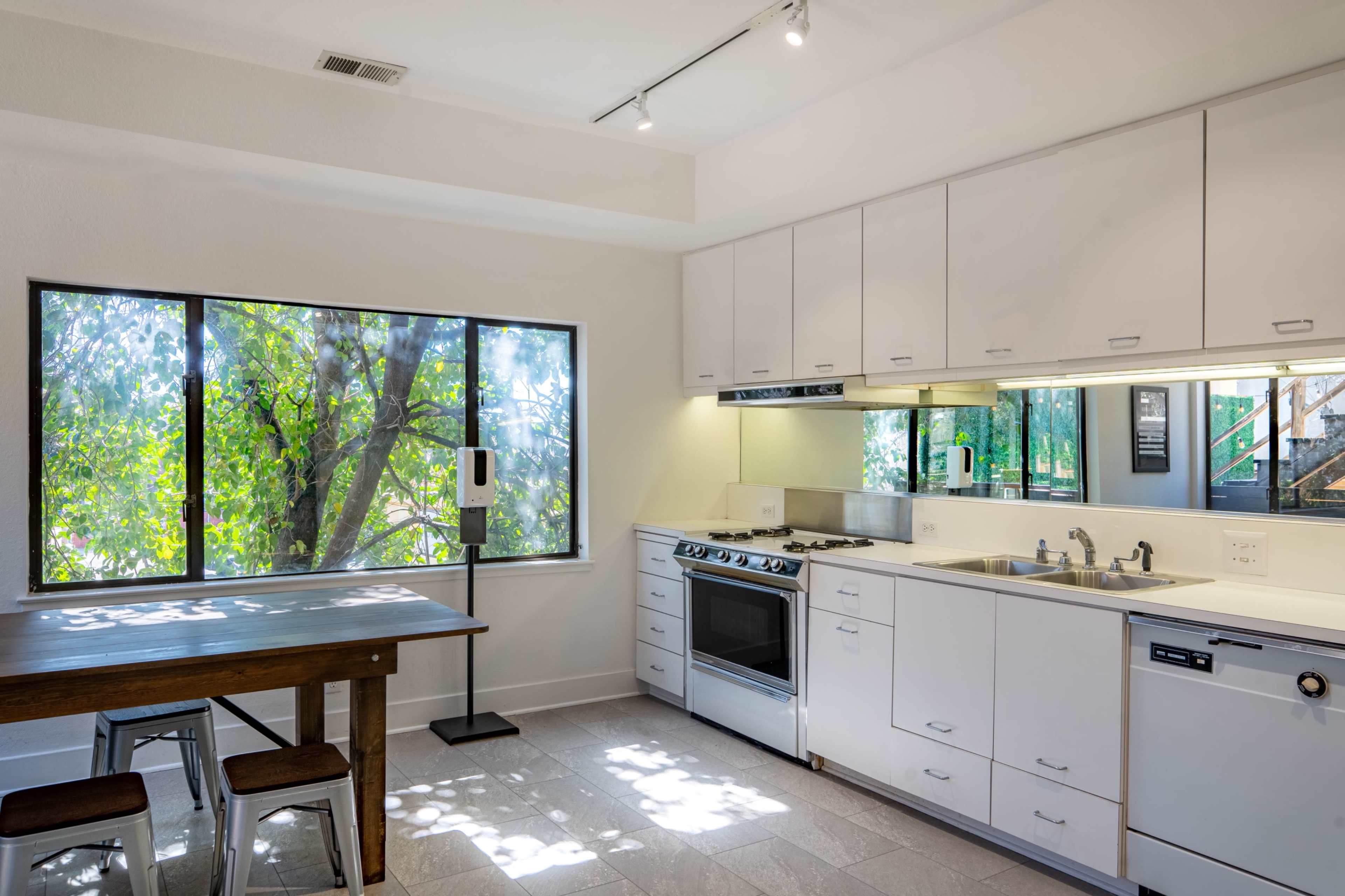 The kitchen features white cabinetry, stainless steel appliances, and a dining area beside a large window overlooking greenery.