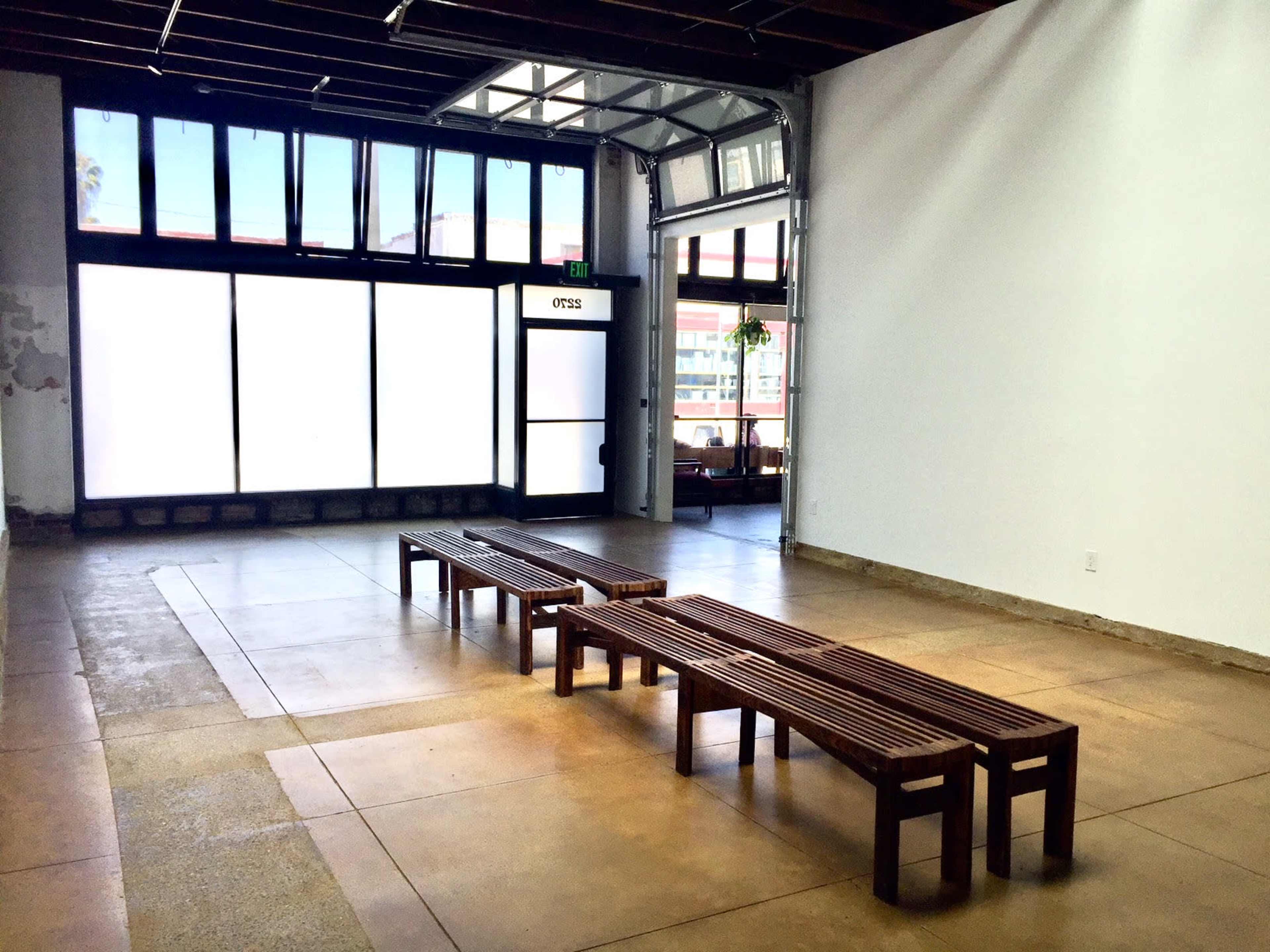 A spacious, minimalistic interior with two wooden benches facing a large glass door and windows.