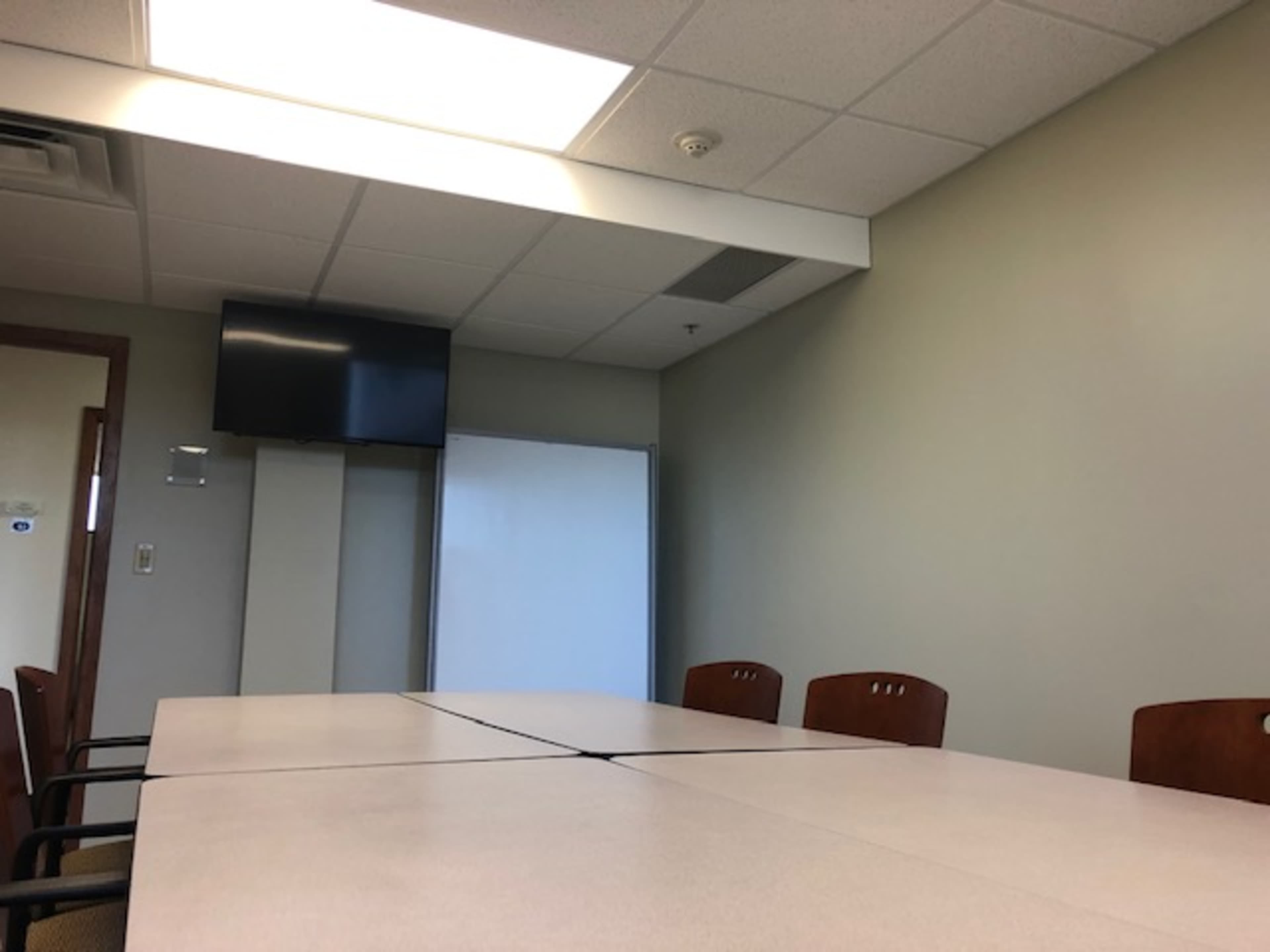 A conference room with a large table, chairs, a flat-screen TV mounted on the wall, and a whiteboard on the side.