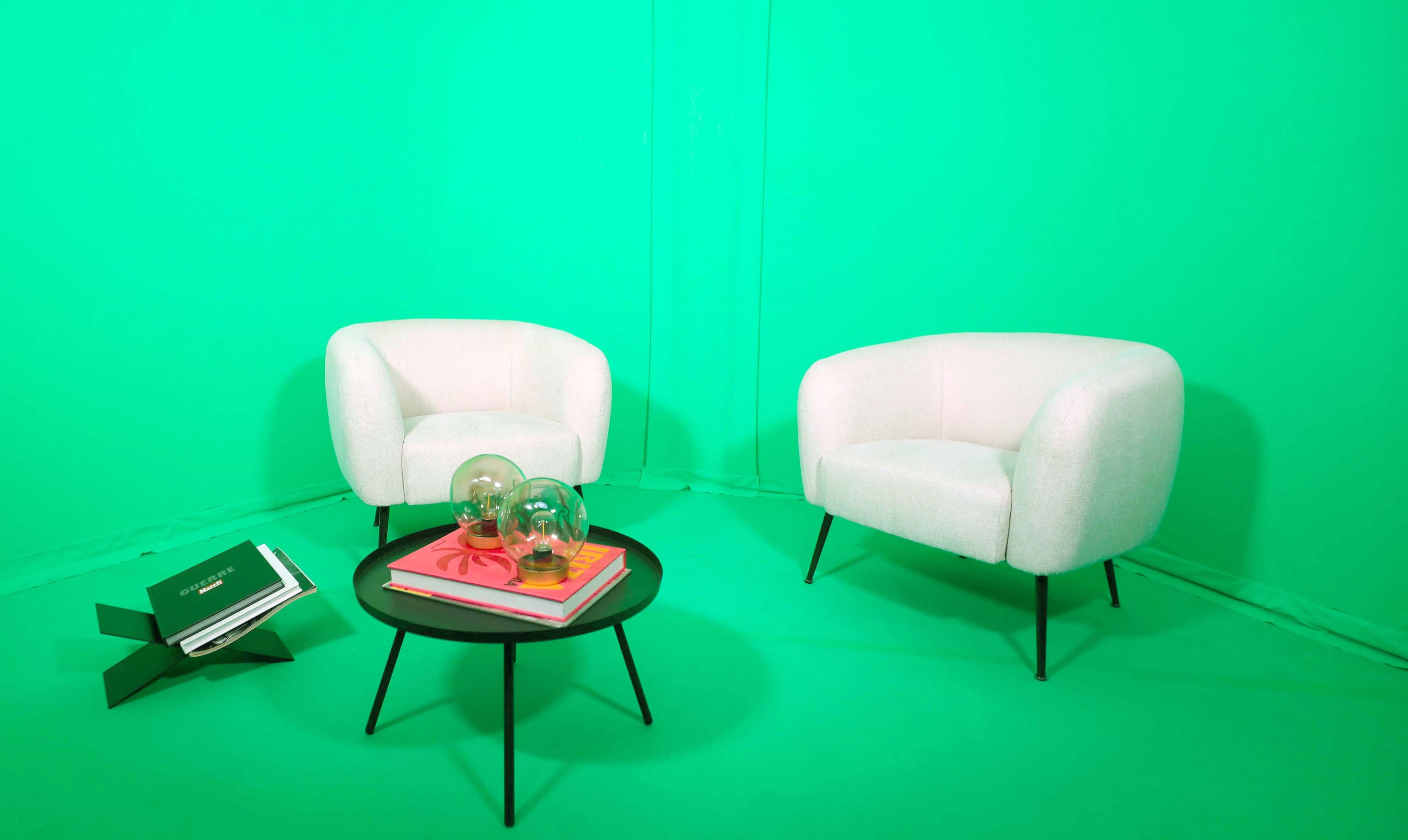 The image features two white armchairs facing a black coffee table, placed on a bright green backdrop.