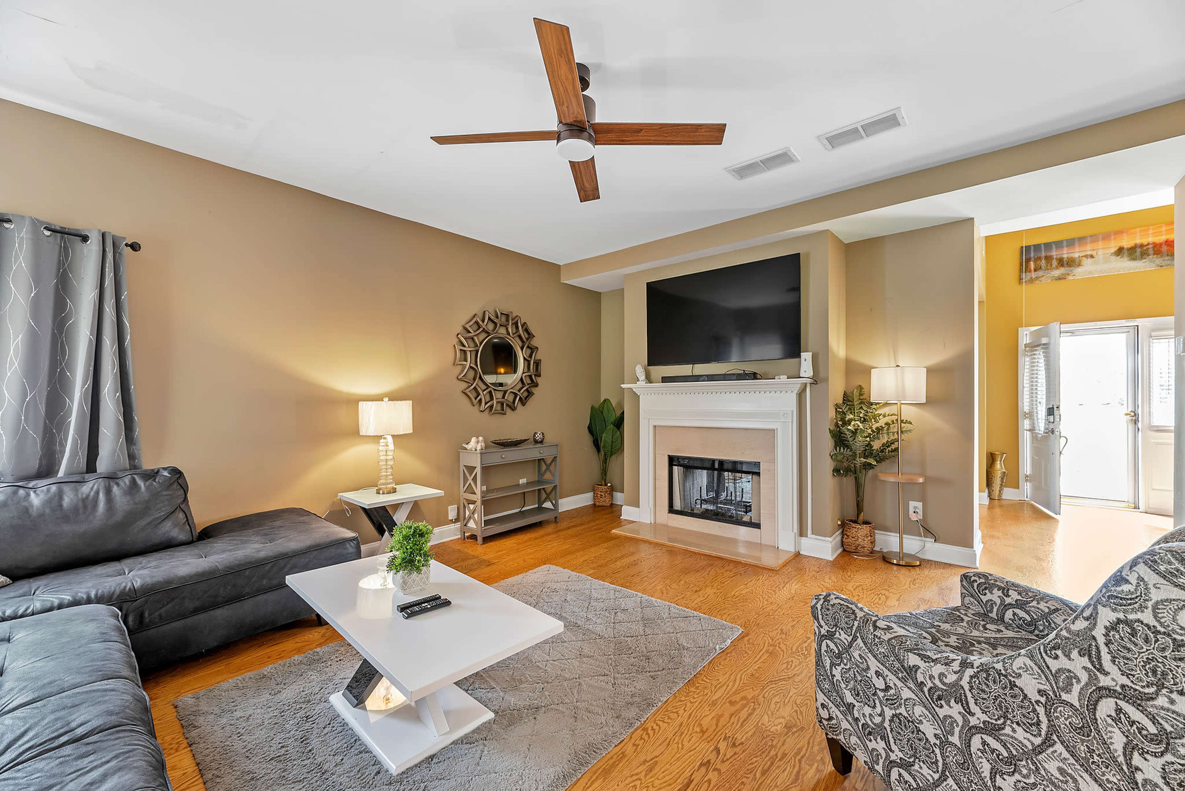 A living room features a sectional sofa, a fireplace with a television above, and a small coffee table on a patterned rug.