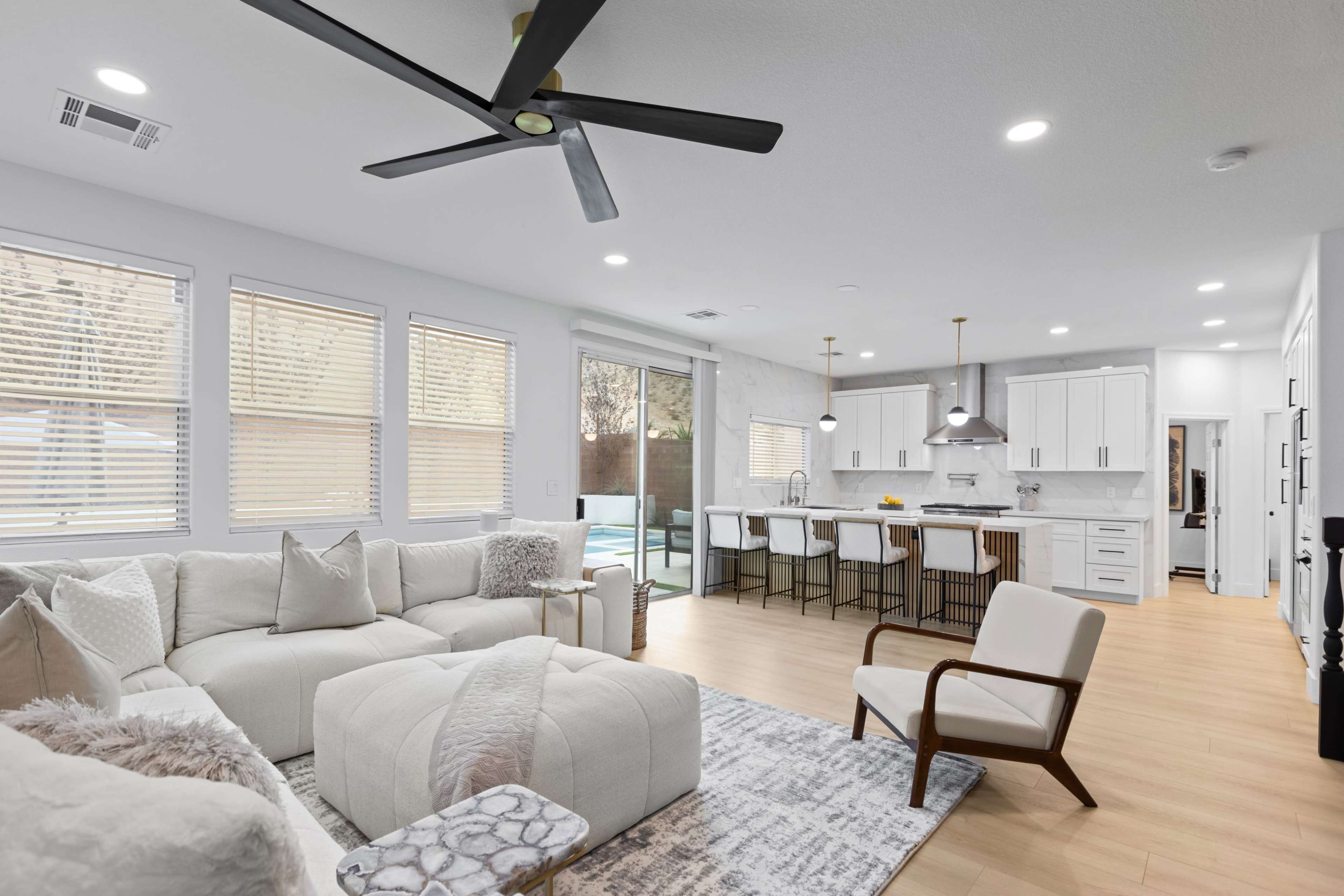 The image features a modern living space with a cream-colored sectional sofa, a minimalist kitchen in the background, and large windows allowing natural light to fill the area.