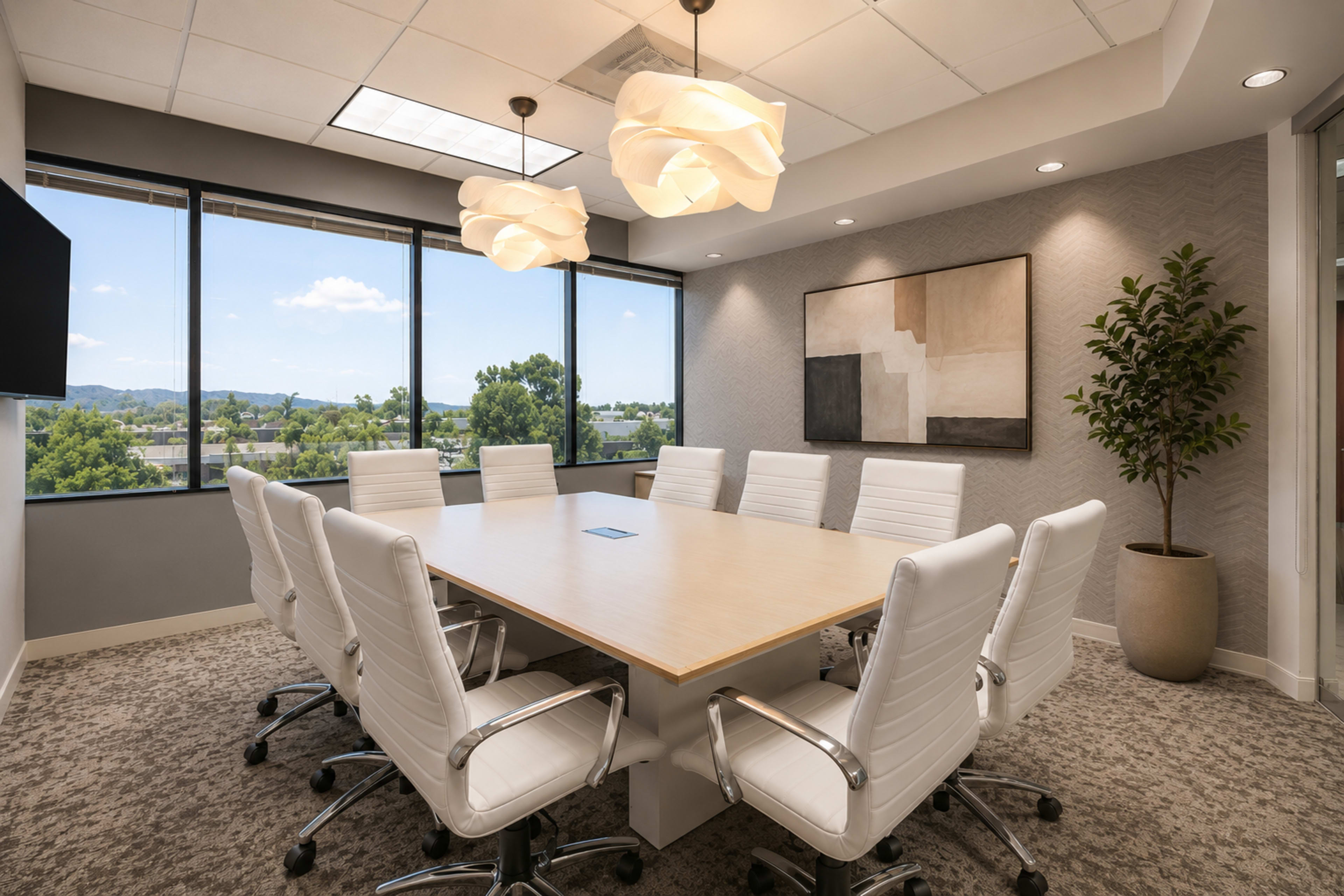 The image shows a bright conference room with a large wooden table surrounded by eight white chairs, large windows, and decorative lighting fixtures.