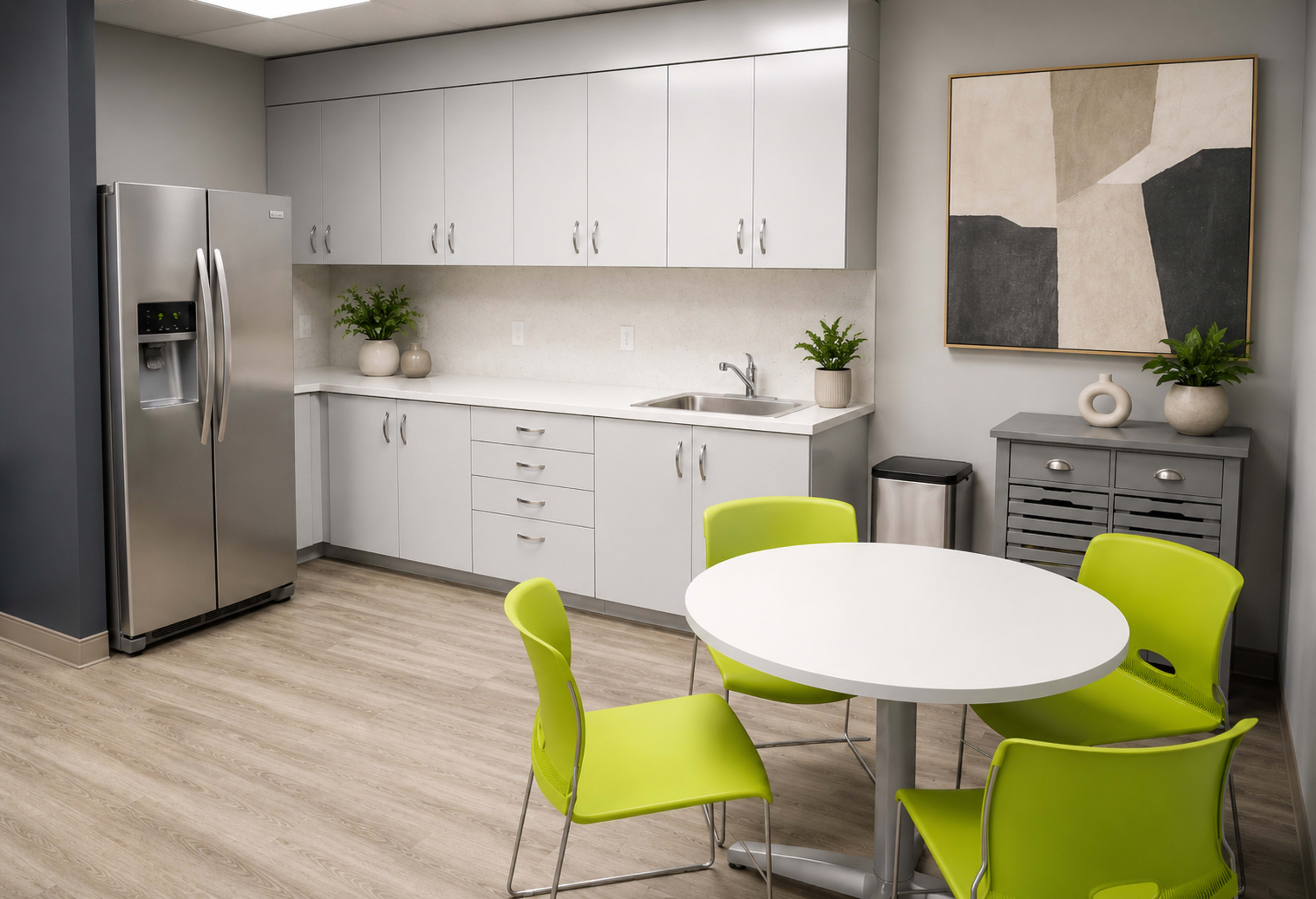 The image shows a modern kitchen area with silver appliances, white cabinetry, a round table, and bright green chairs.