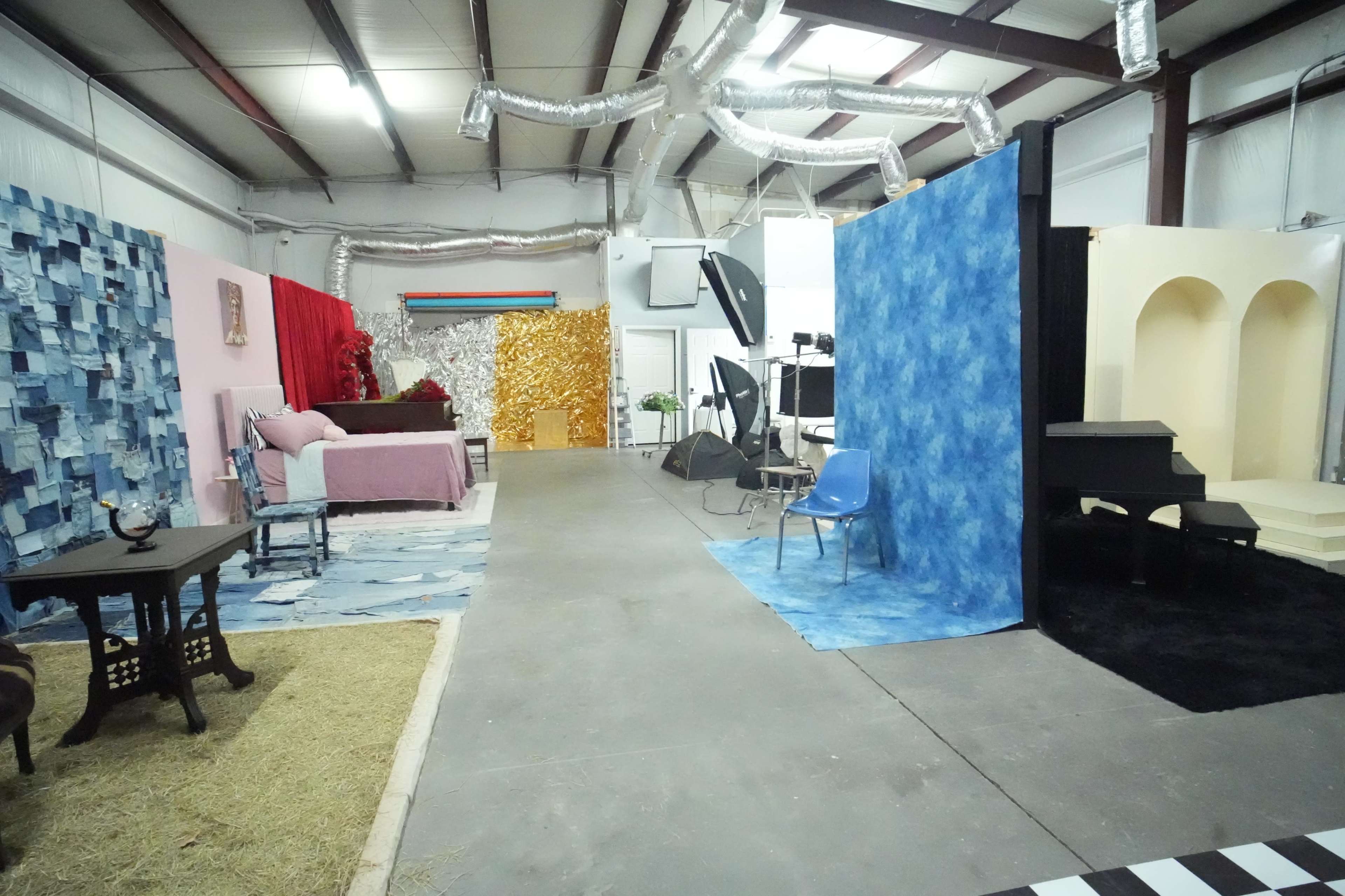 The image shows a large indoor space featuring various styled areas, including a pink and blue setup, a golden backdrop, and a small stage with a piano.