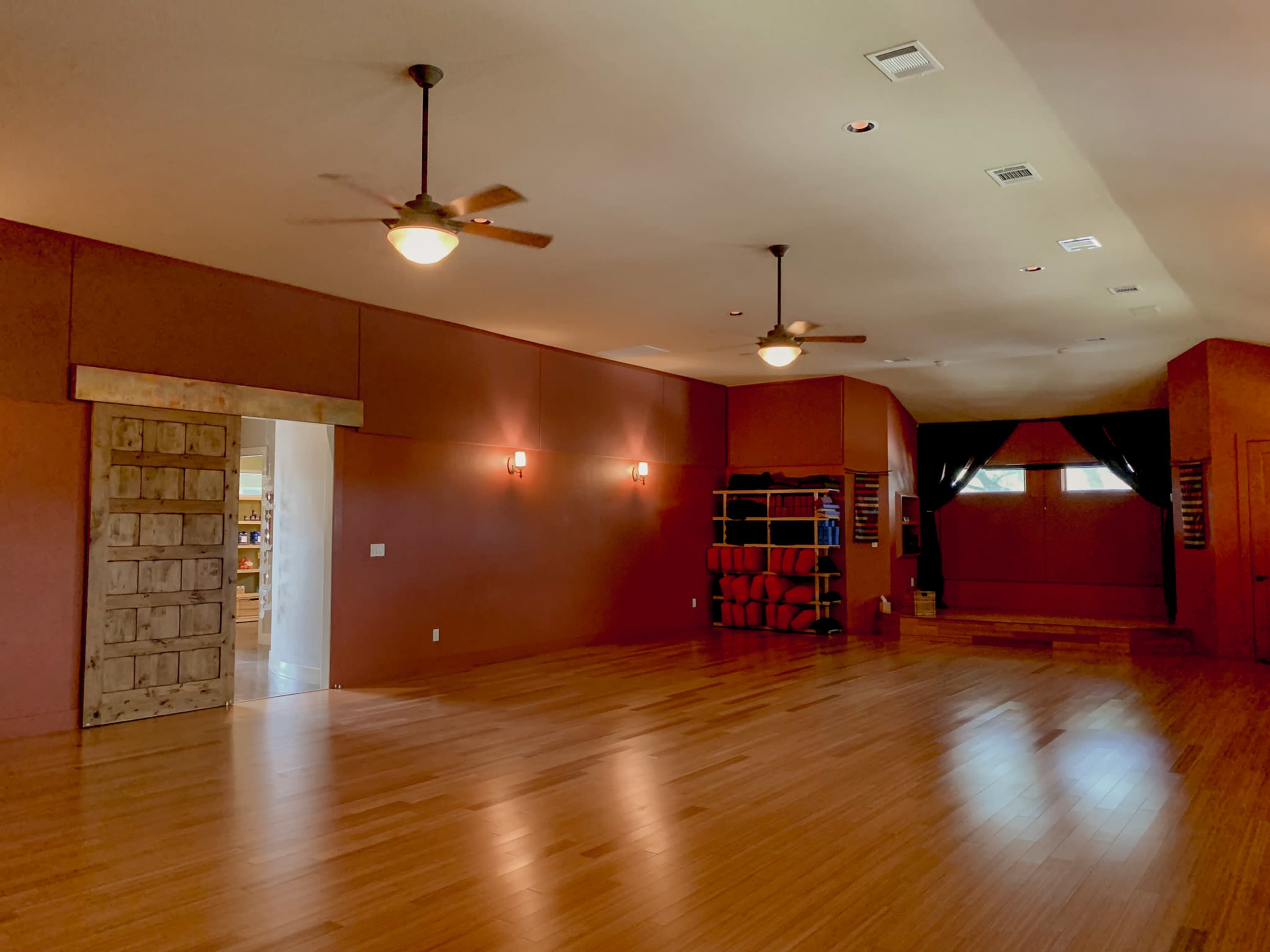 An empty yoga studio with wooden floors, soft lighting, and a doorway leading to another room.