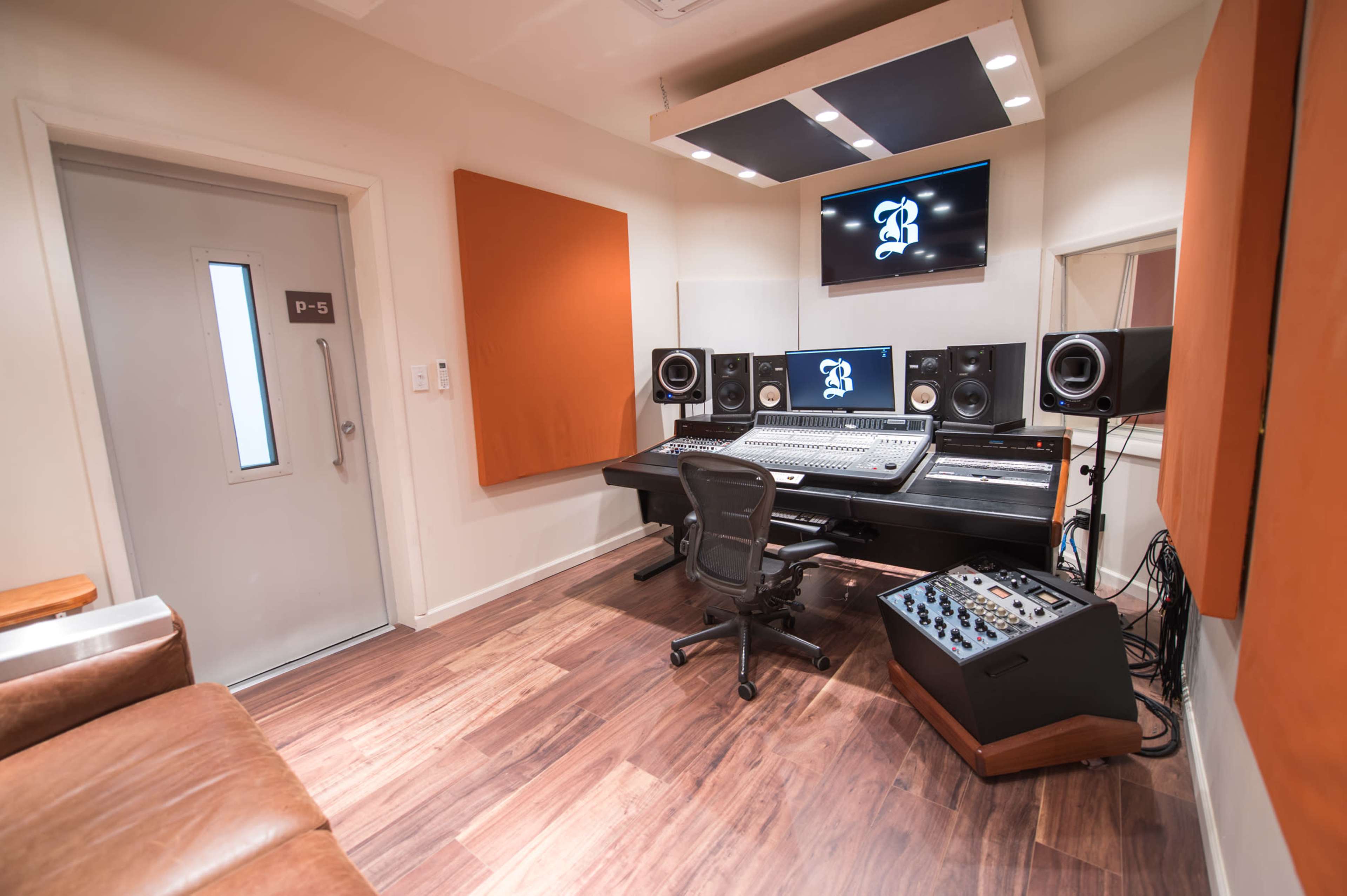 A music studio with a control desk, audio monitors, and a door labeled "P-5."