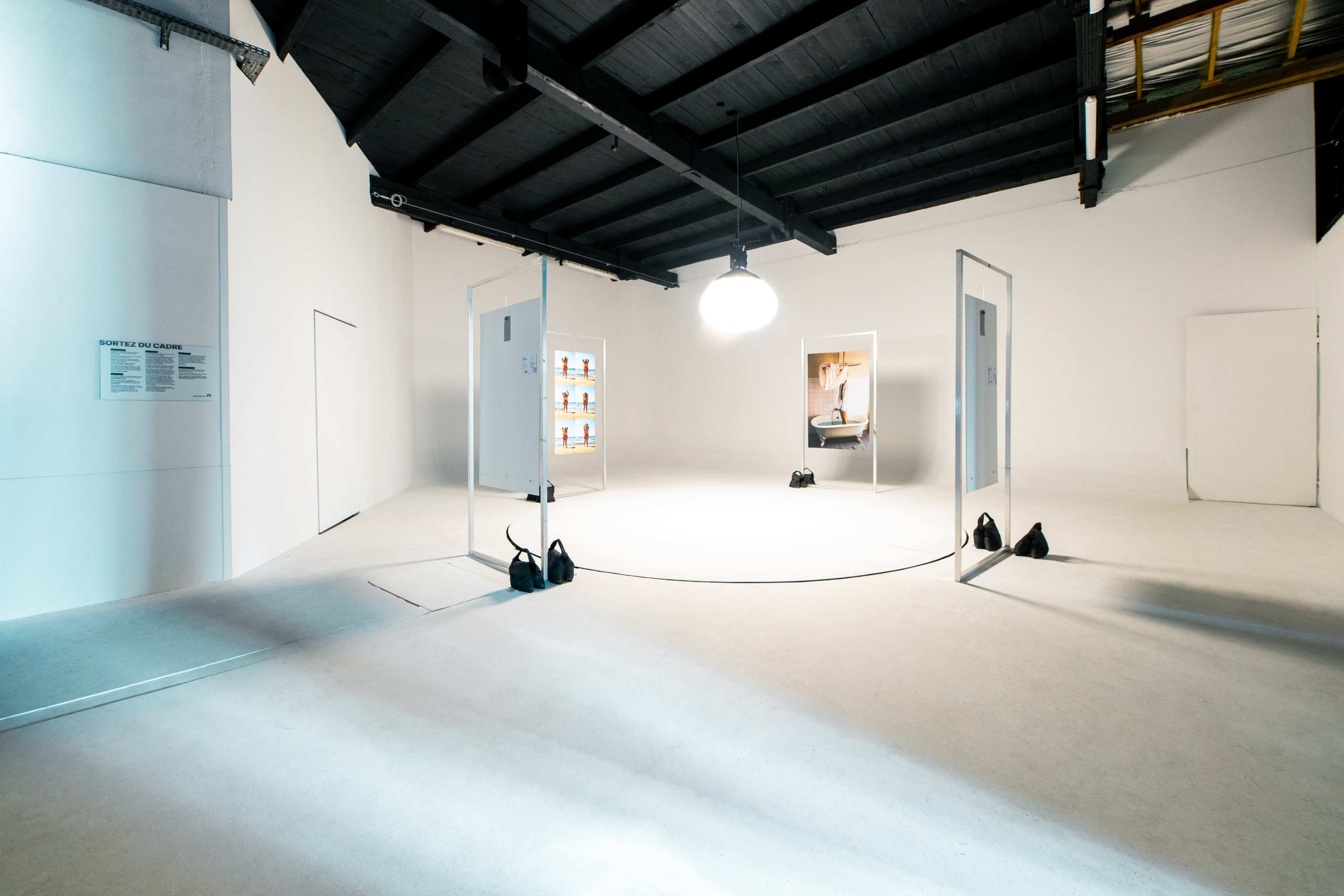 The image shows an empty art gallery with white walls, a circular arrangement of open doors, and illuminated displays featuring artwork.