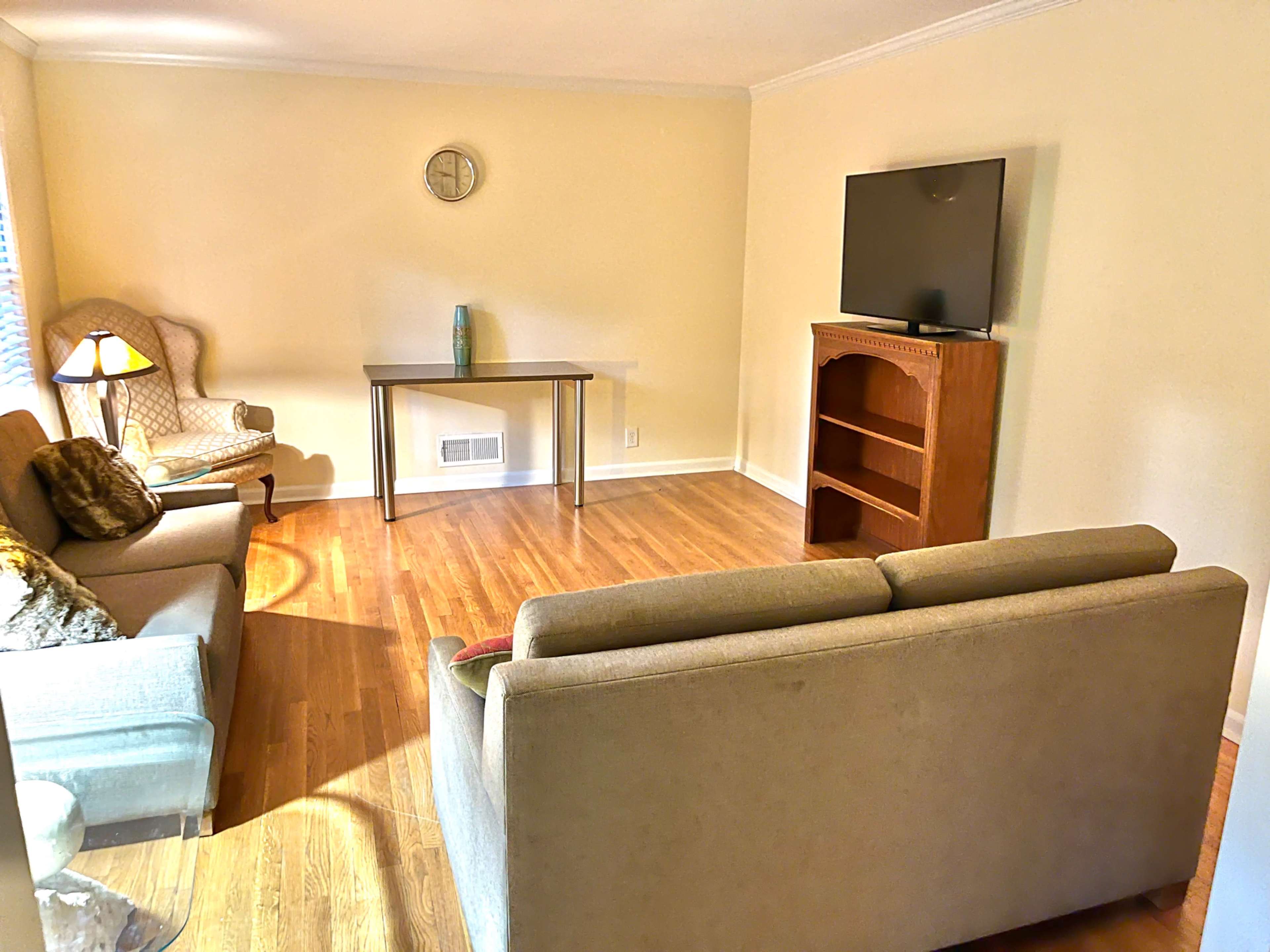 The image shows a living room with two sofas, a small table against the wall, a television on a wooden stand, and a chair in the corner.
