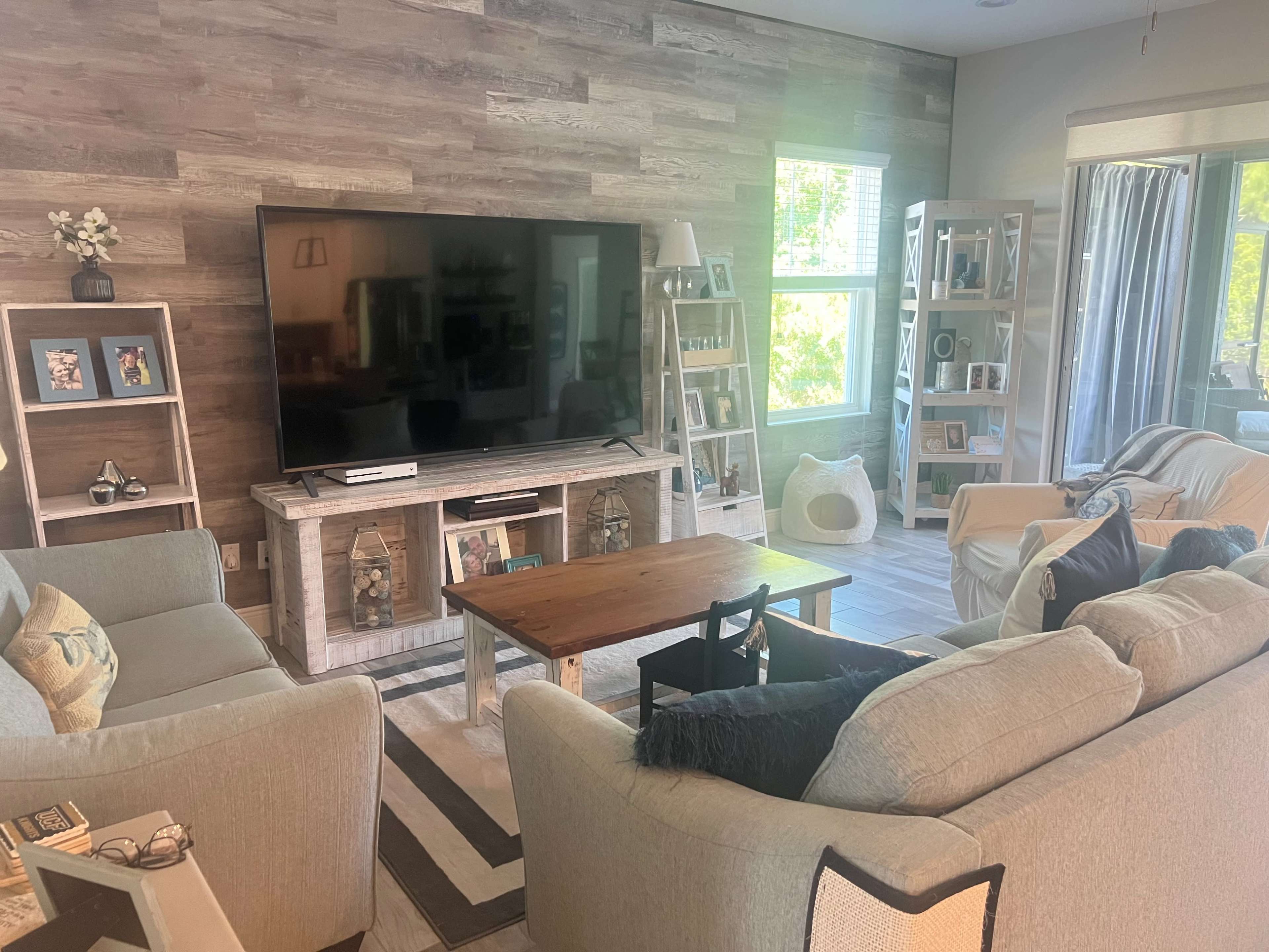 The living room features a large television mounted on a wooden wall with a coffee table in front of a sectional sofa and armchairs arranged around it.