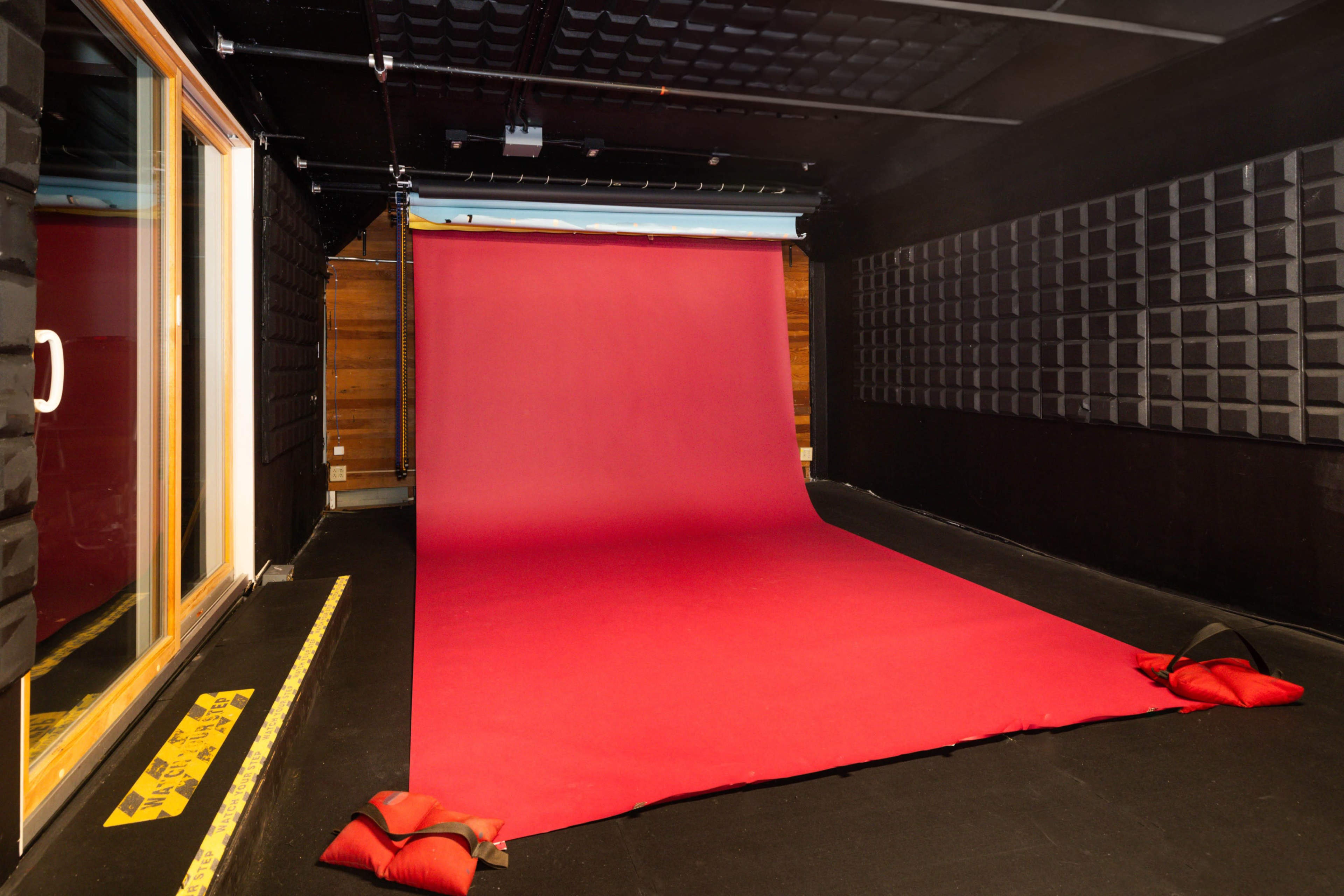 The image shows a soundproof room featuring a large red backdrop on the floor, with padded weights holding it down.