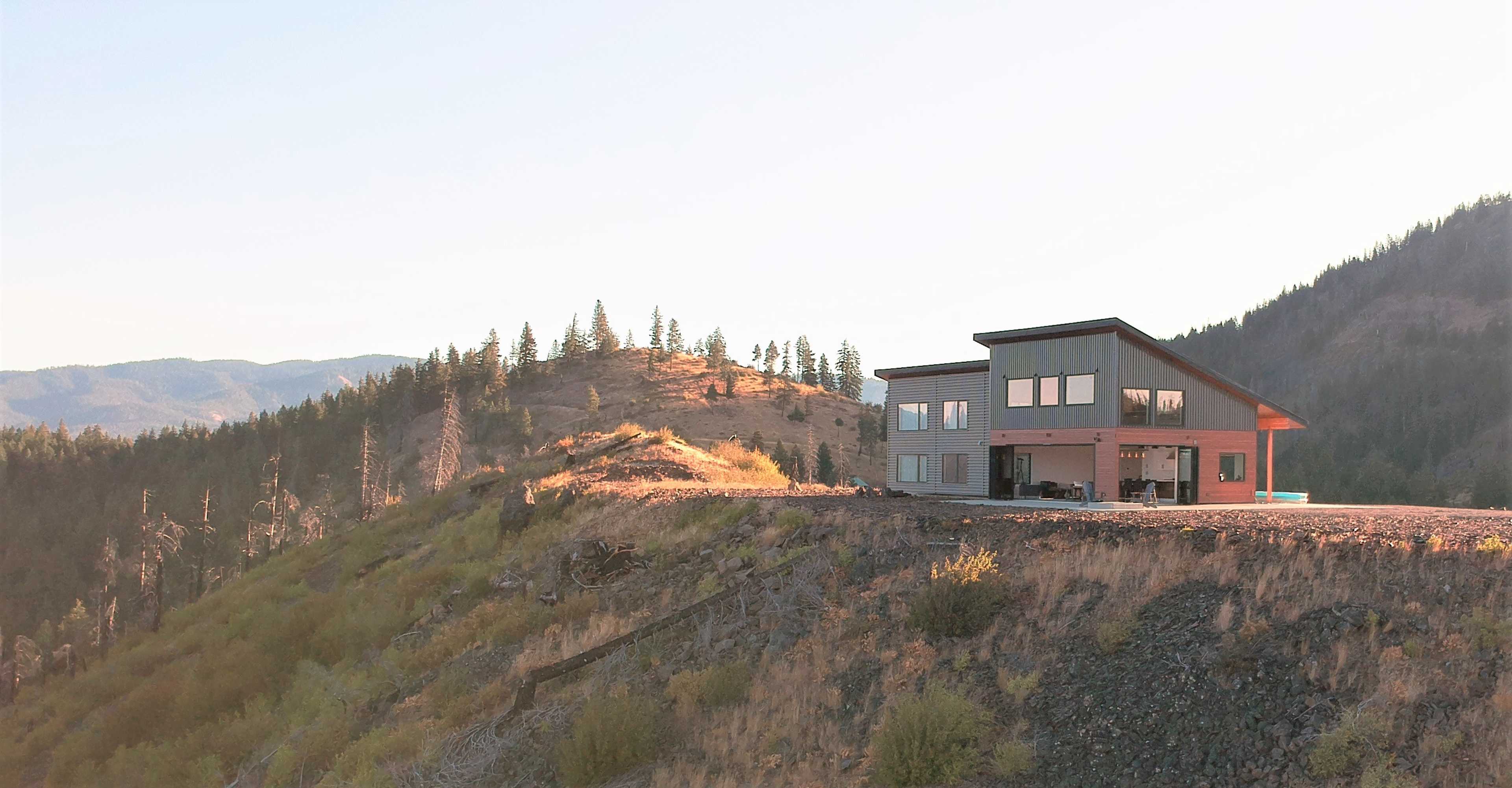 A modern house is situated on a hillside overlooking a mountainous landscape.