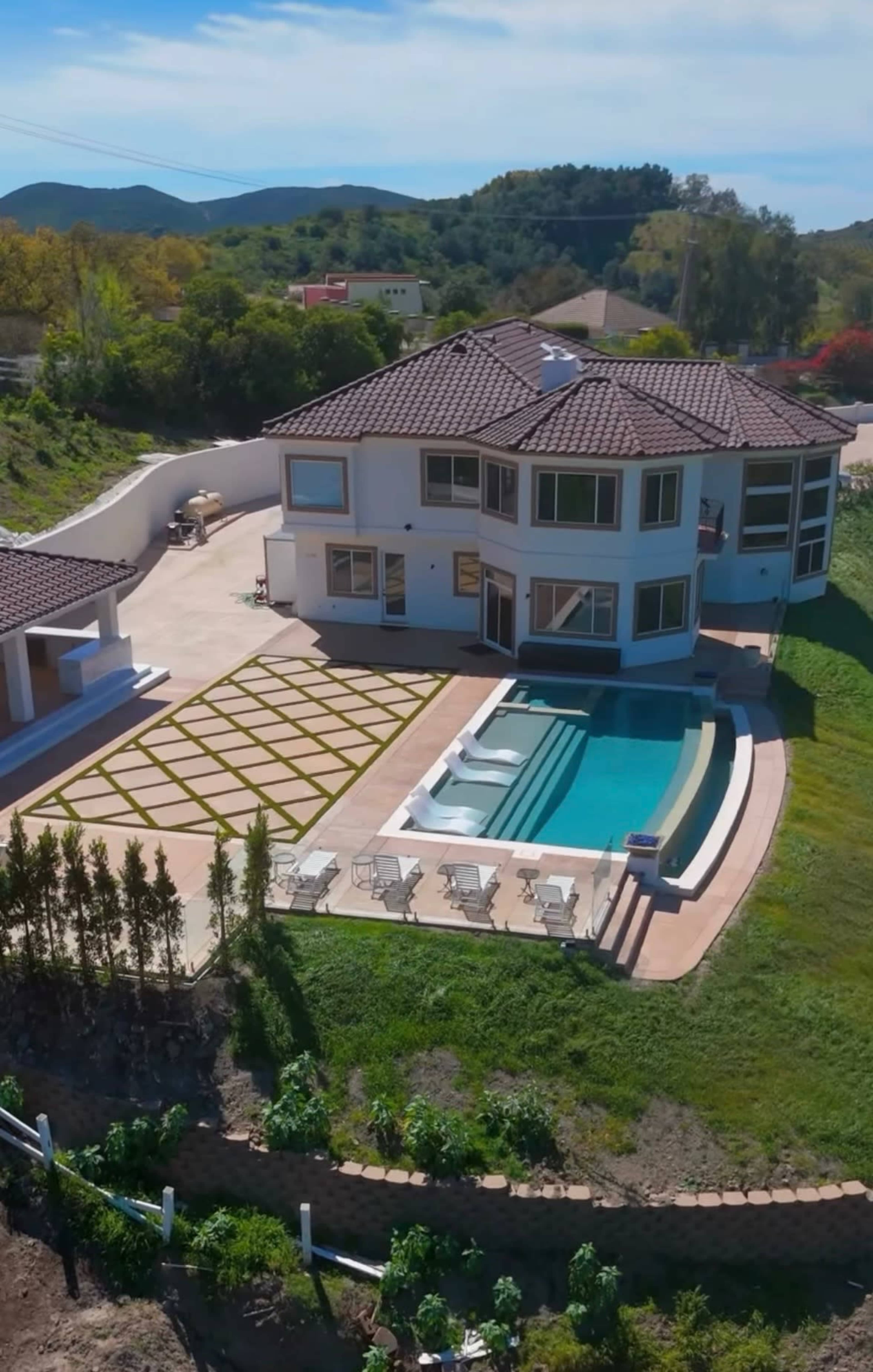 A modern two-story house with a swimming pool and landscaped yard is situated on a hillside.