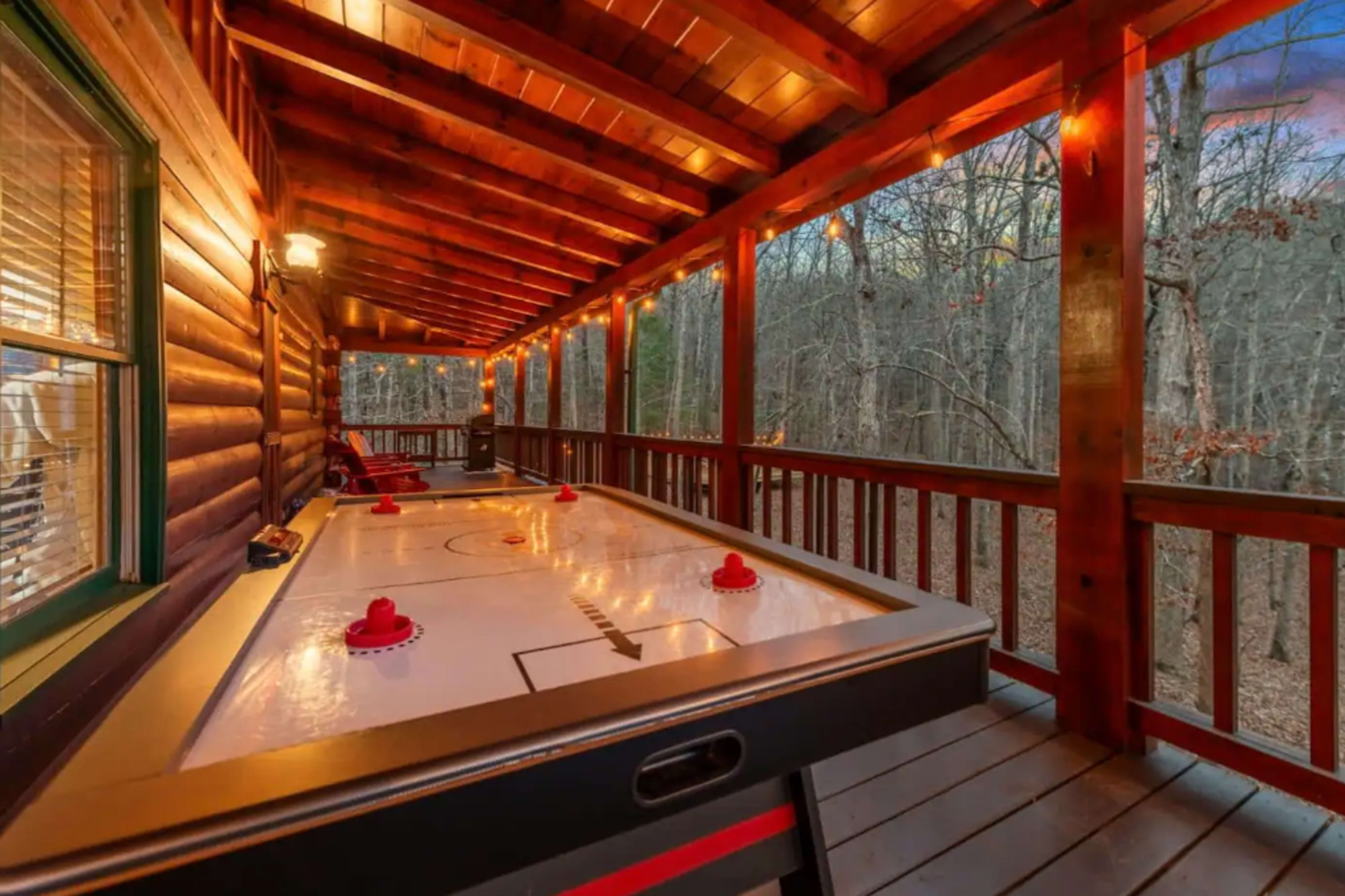 A wooden porch with an air hockey table set up, surrounded by trees and string lights illuminating the area.