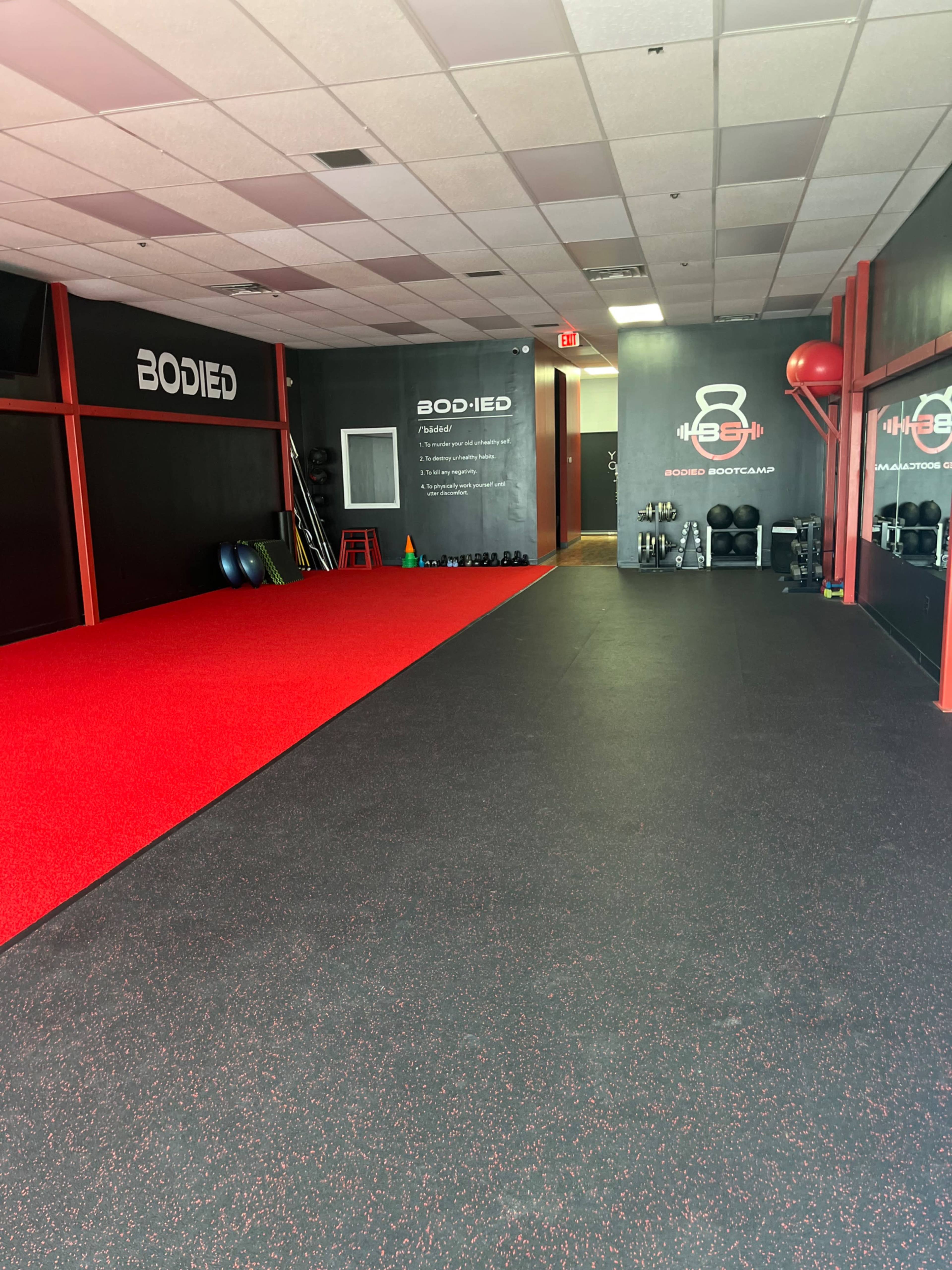 A fitness studio with red and black rubber flooring, equipped with various workout equipment along the walls.