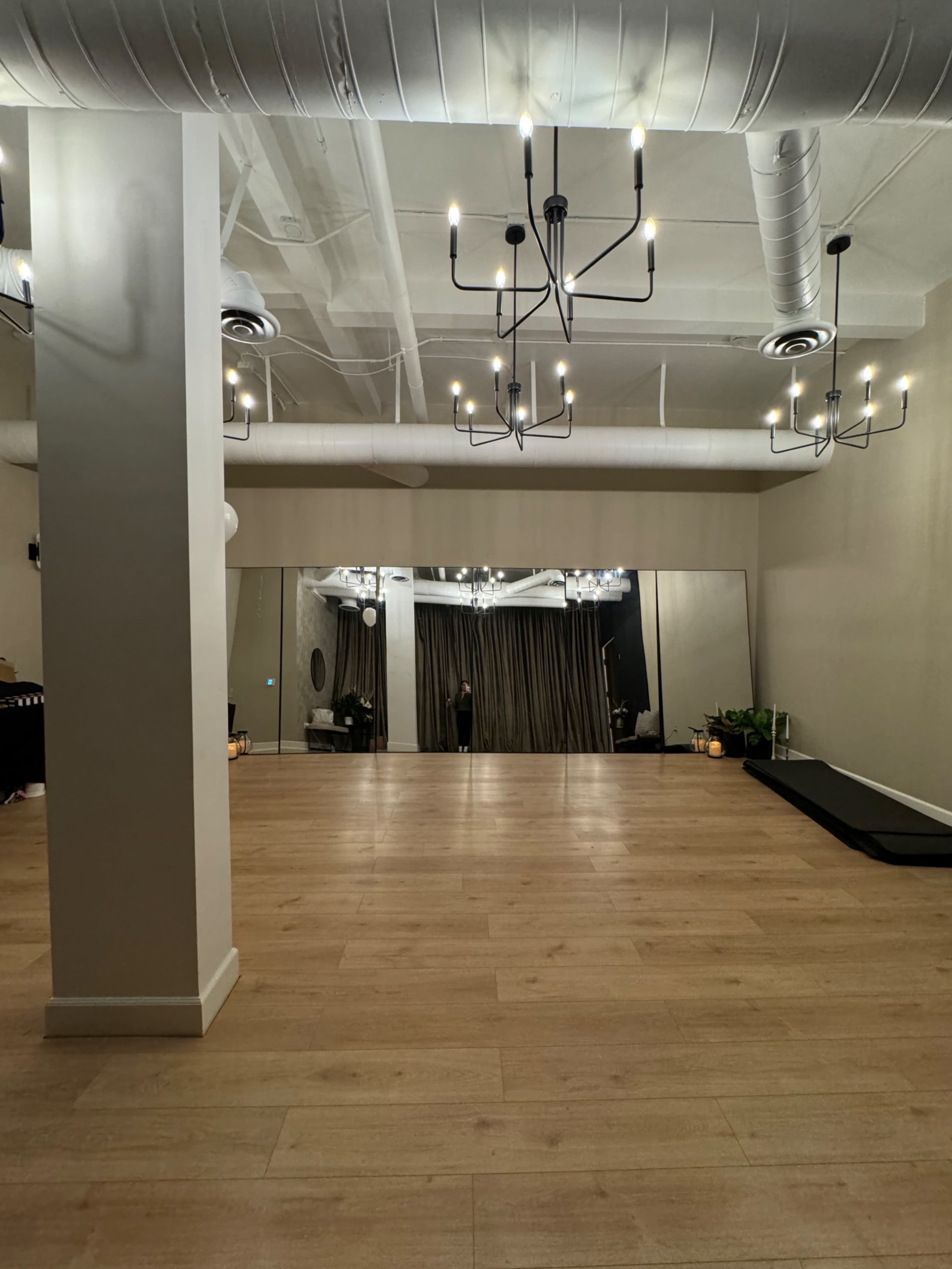 The scene features a spacious, well-lit room with wooden flooring, mirrored walls, and chandeliers hanging from the ceiling.