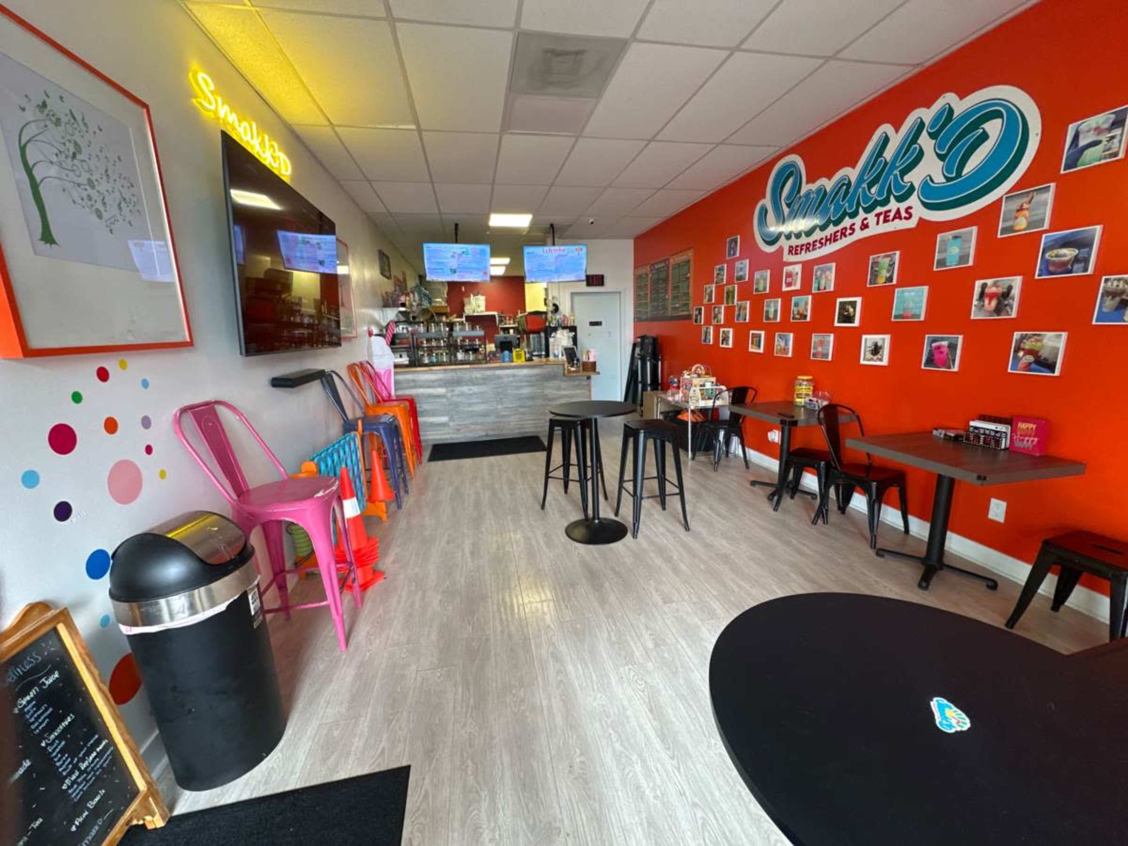 The interior of a bright café features colorful chairs, a service counter, and walls adorned with framed photos.