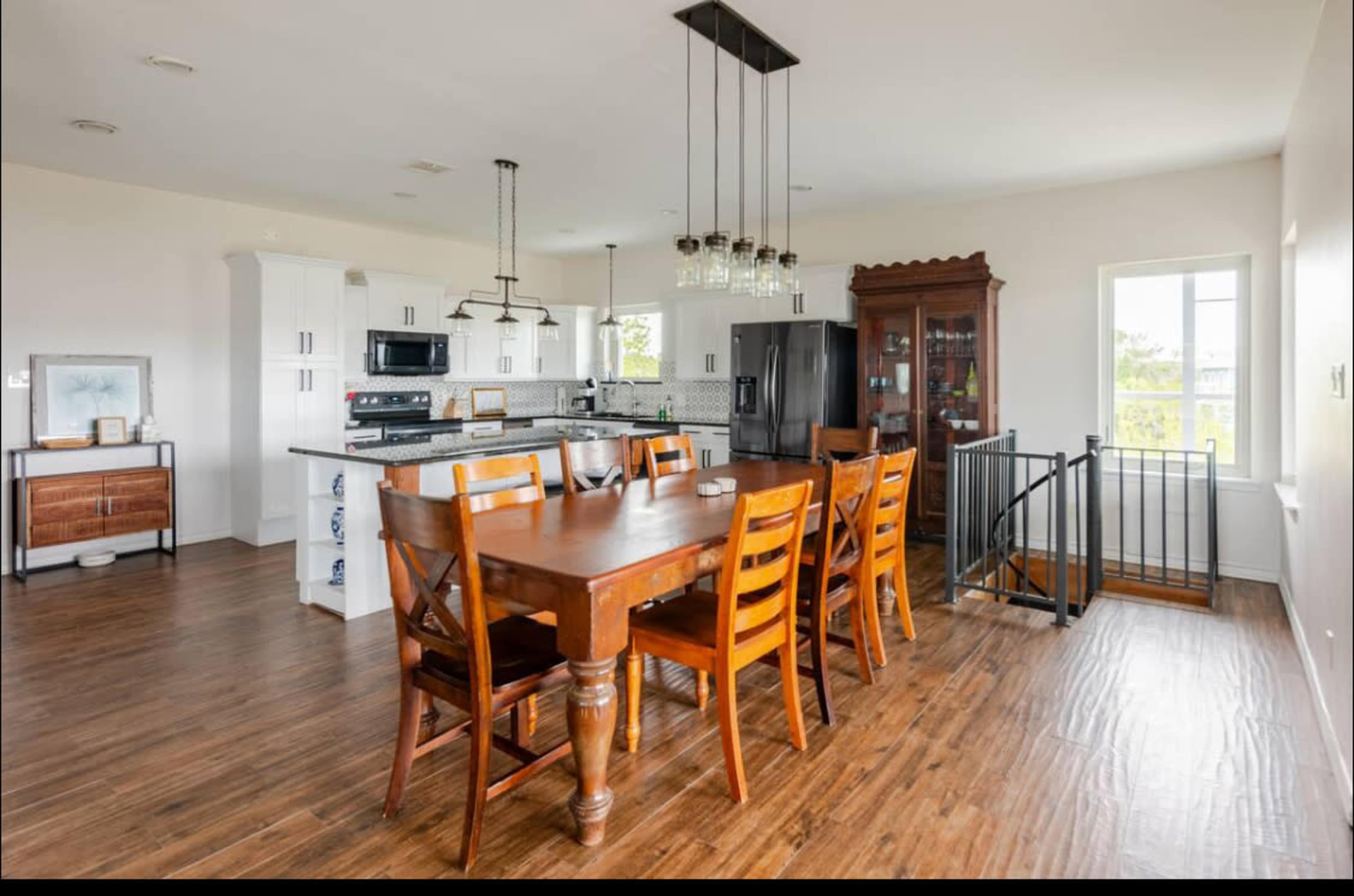 A spacious kitchen and dining area feature a wooden dining table with six chairs, modern appliances, and a large window allowing natural light.