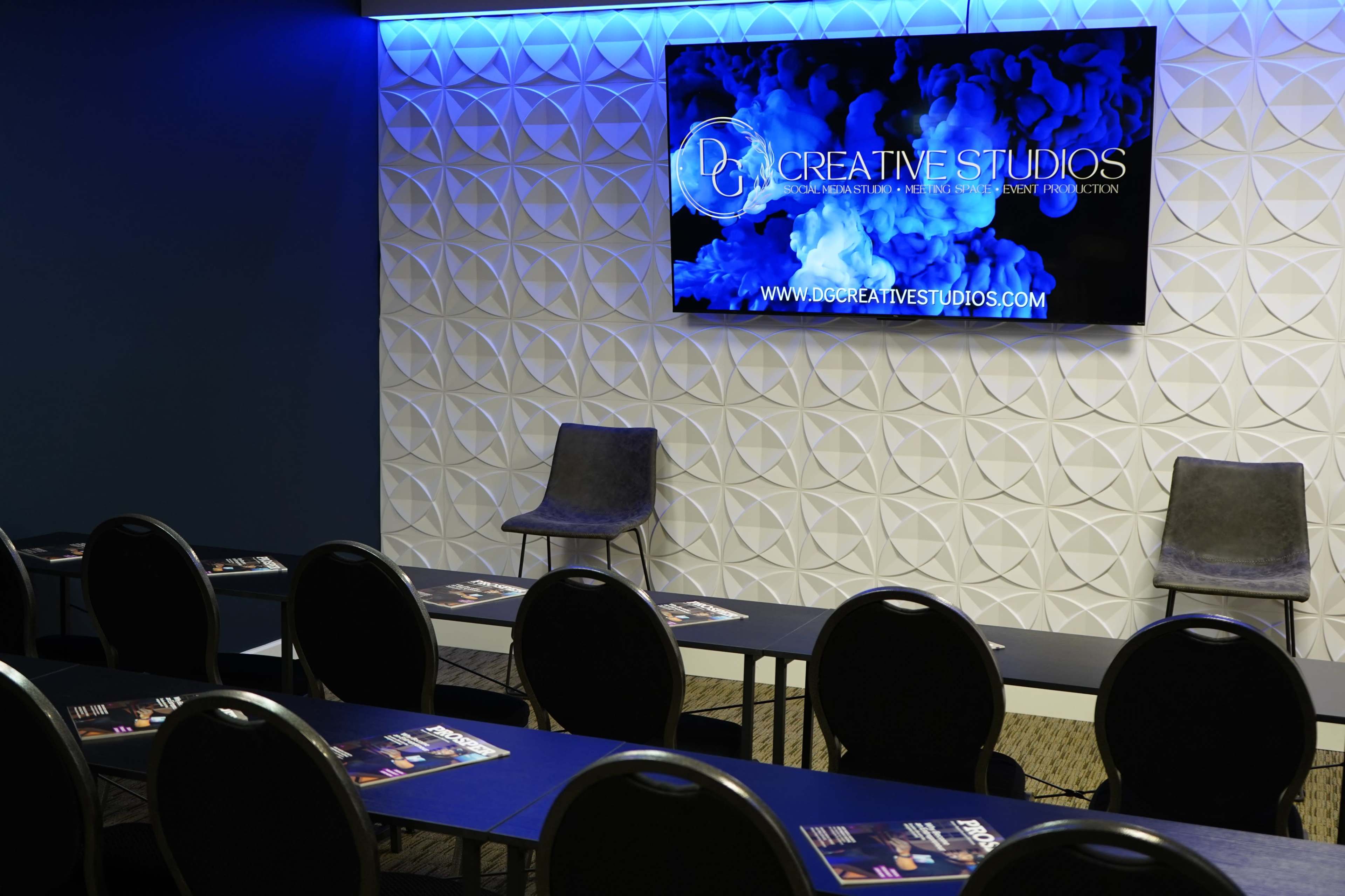 A modern presentation room with gray chairs, a large screen displaying a logo, and neatly arranged tables.