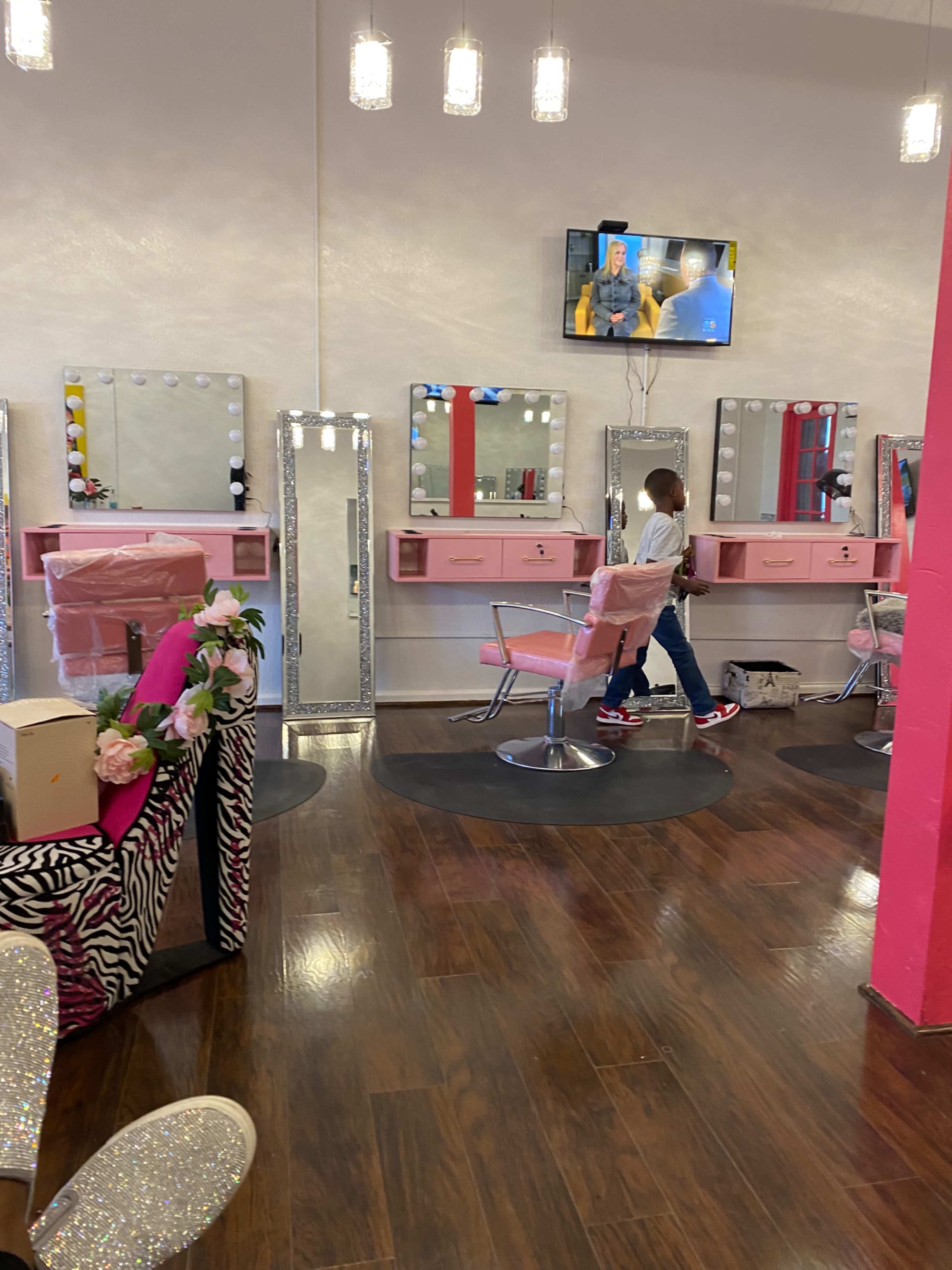 The image shows a brightly lit hair salon with multiple mirrors, pink styling chairs, and a television on the wall.