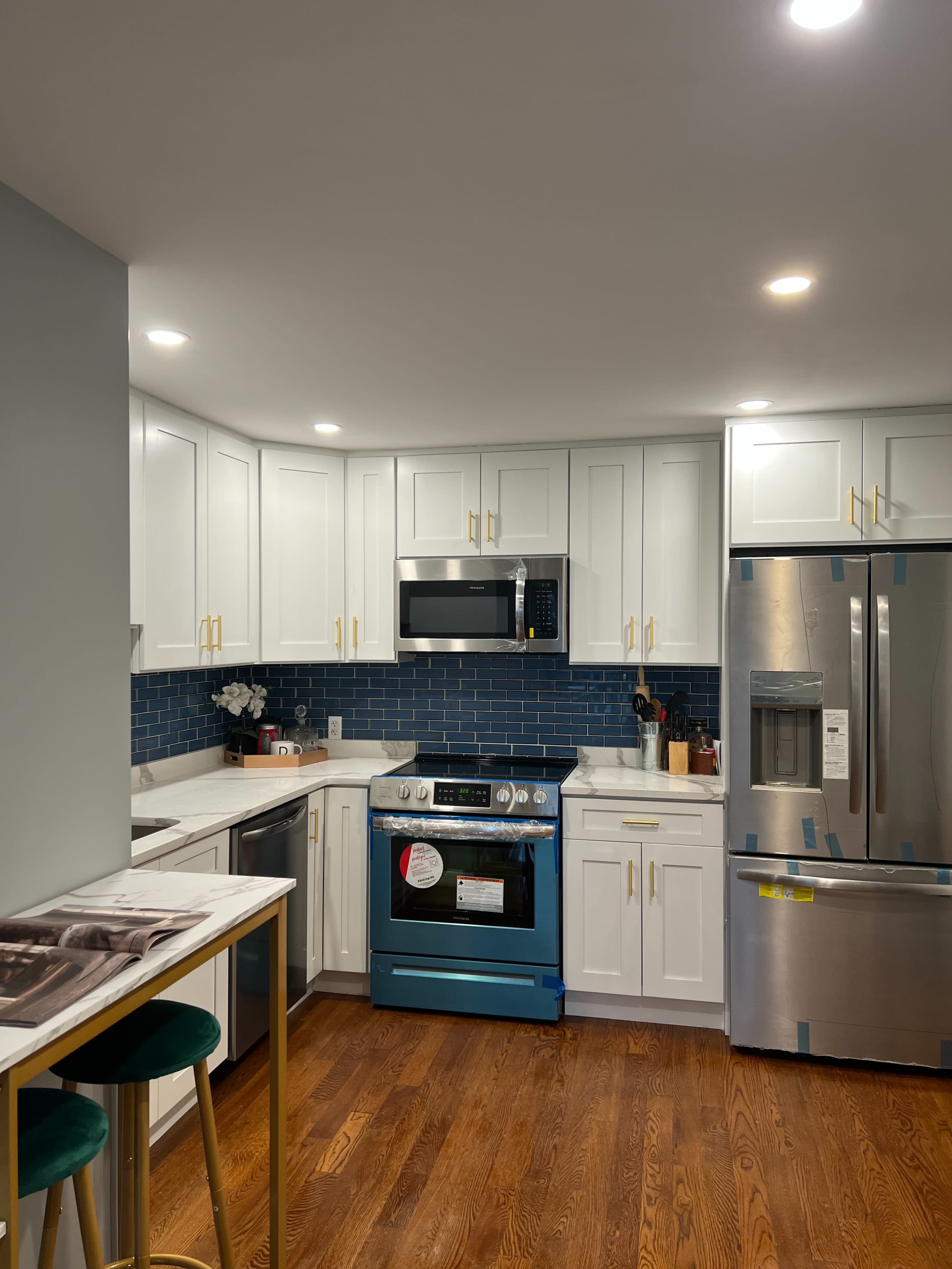 A modern kitchen with white cabinets, a blue tile backsplash, stainless steel appliances, and wooden flooring.