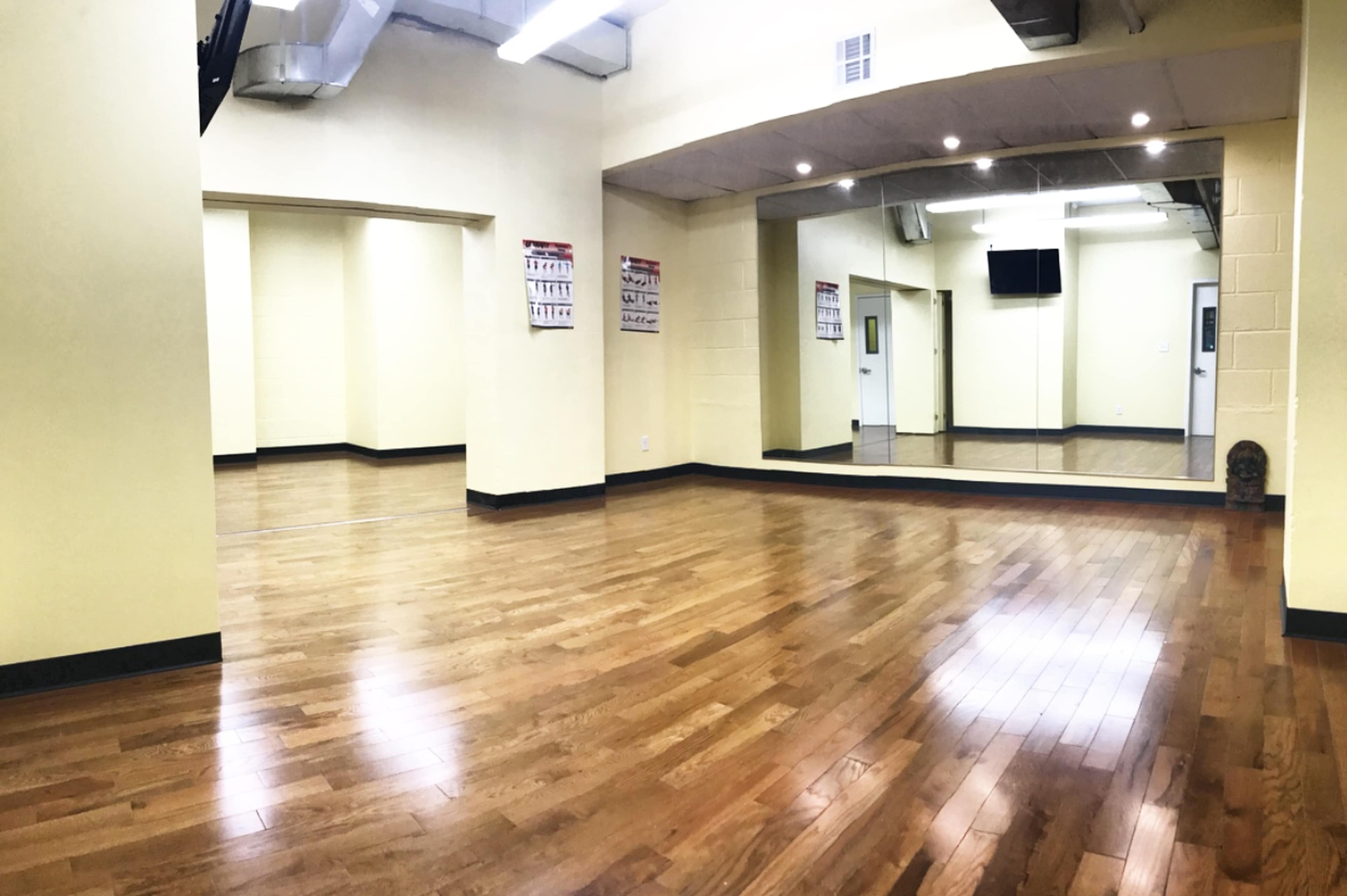 A spacious, empty room with yellow walls, wooden flooring, and a large mirror along one wall.