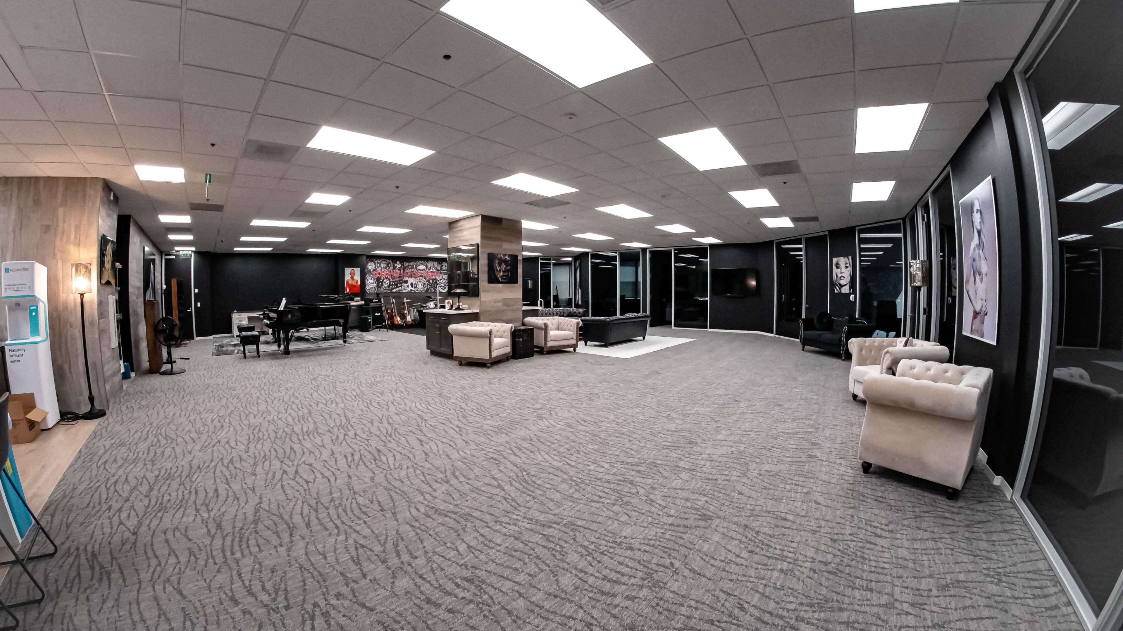 A spacious office interior featuring a piano, several couches, and large windows with a view.
