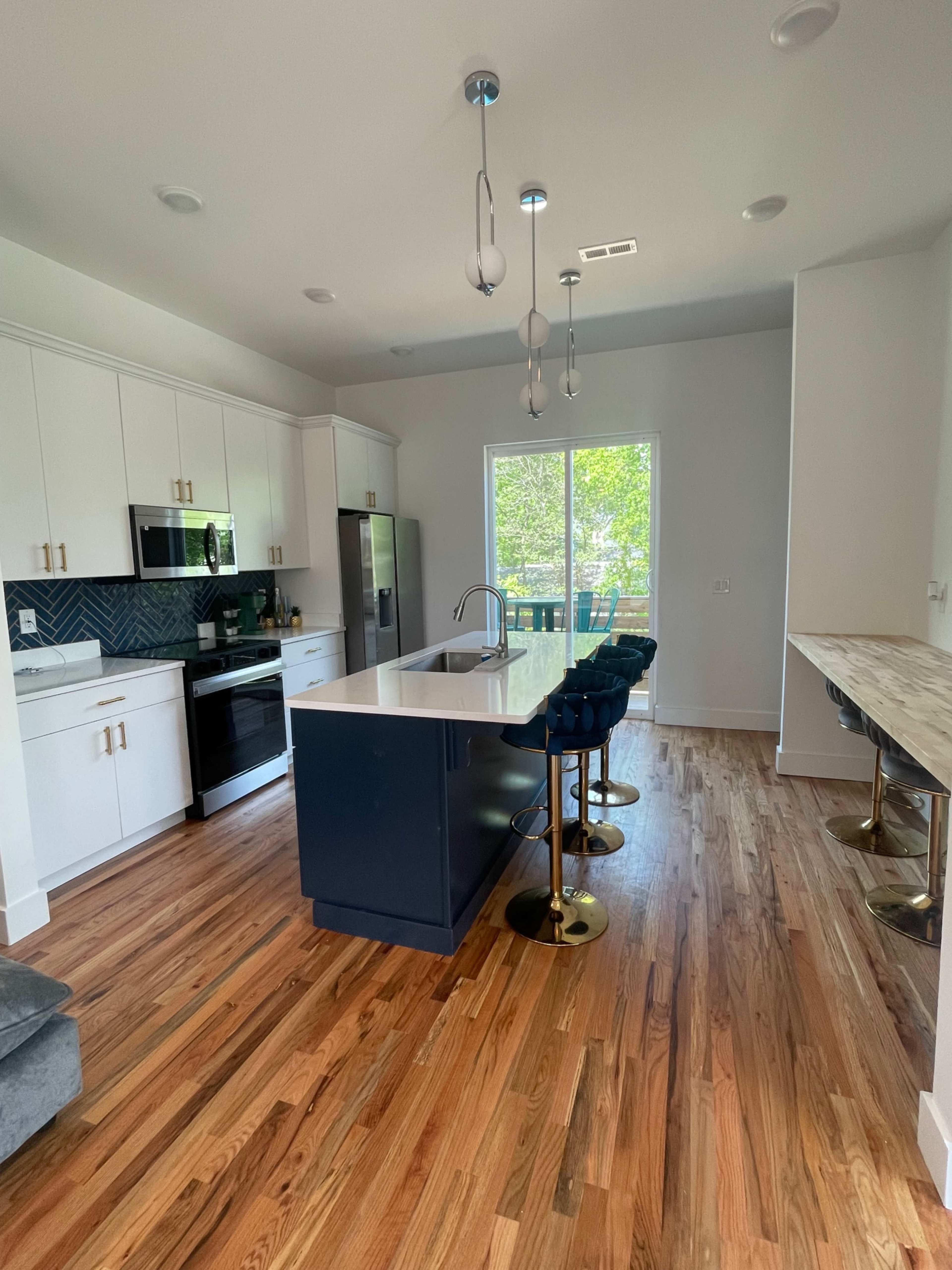 The image shows a modern kitchen featuring white cabinetry, stainless steel appliances, a large island with seating, and hardwood flooring.
